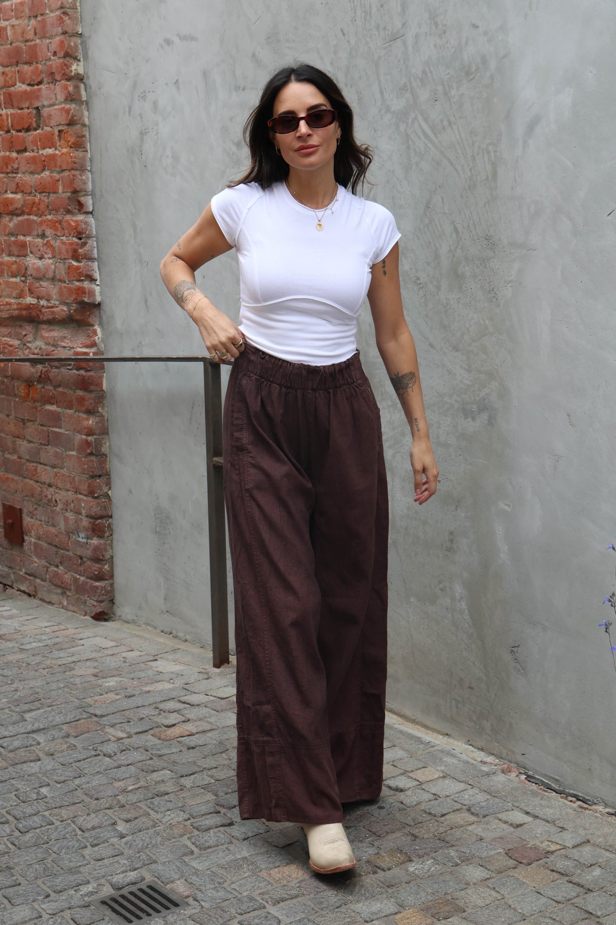 woman wearing brown linen pants against a grey background
