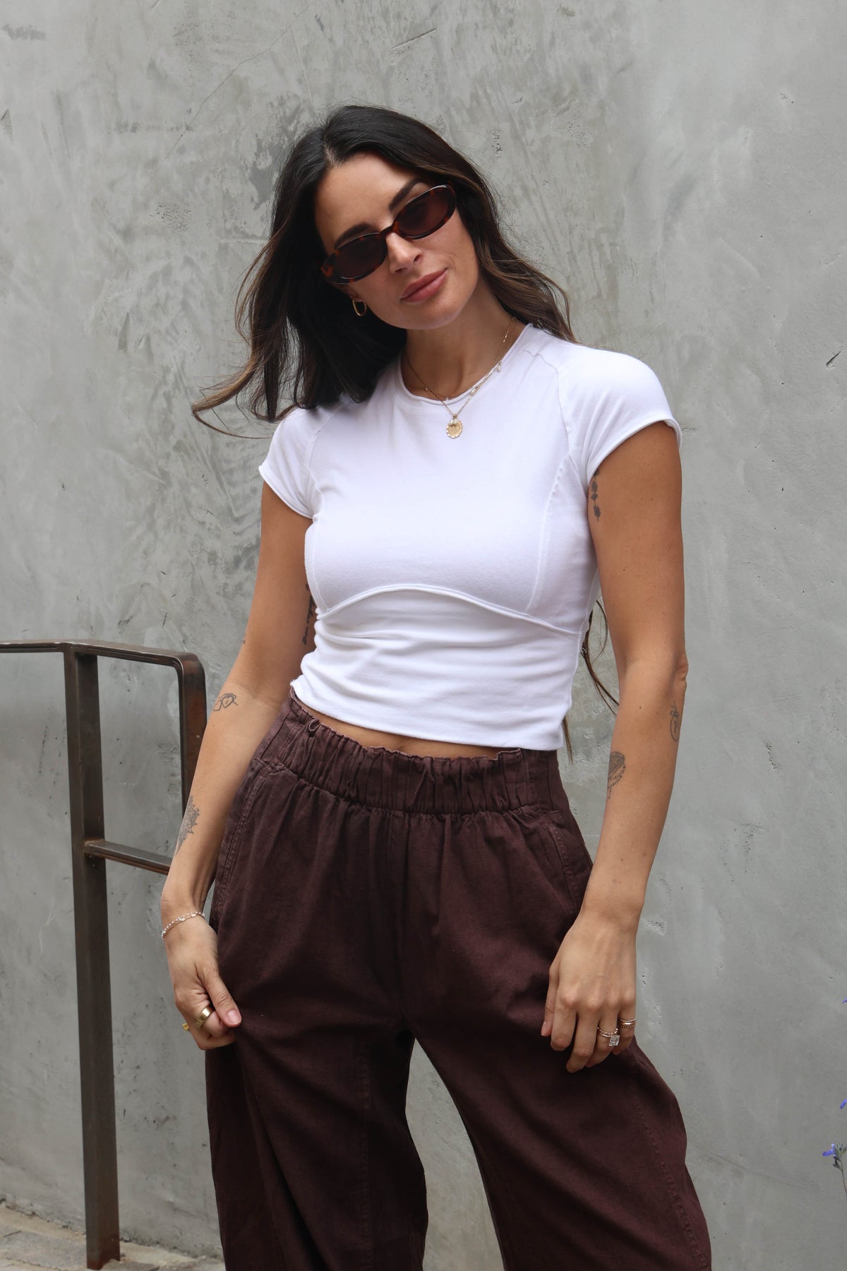 Woman wearing a white top and brown linen pants against a grey background