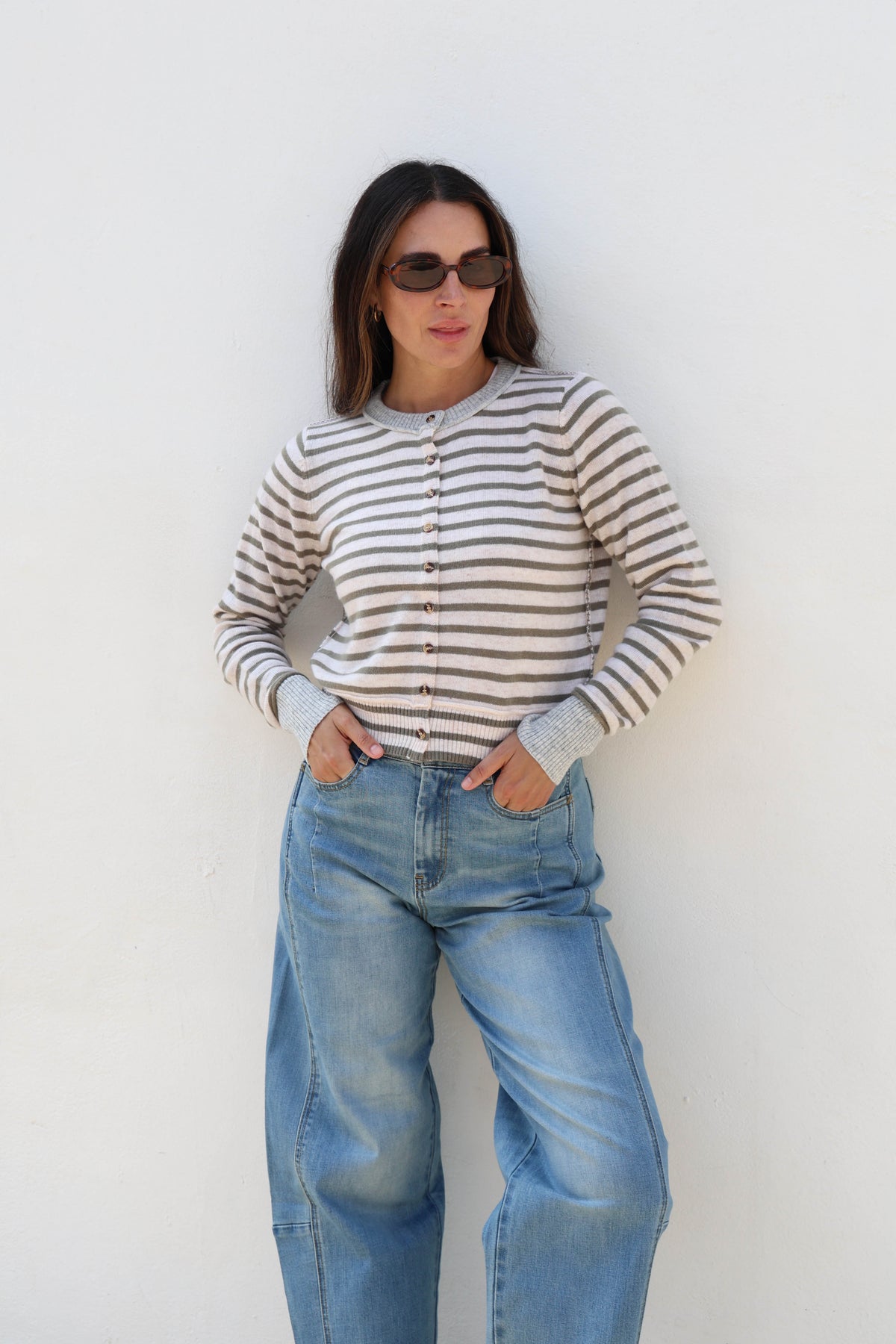 A woman wearing a ribbed knit cardigan with horizontal gray and off-white stripes, paired with blue jeans.