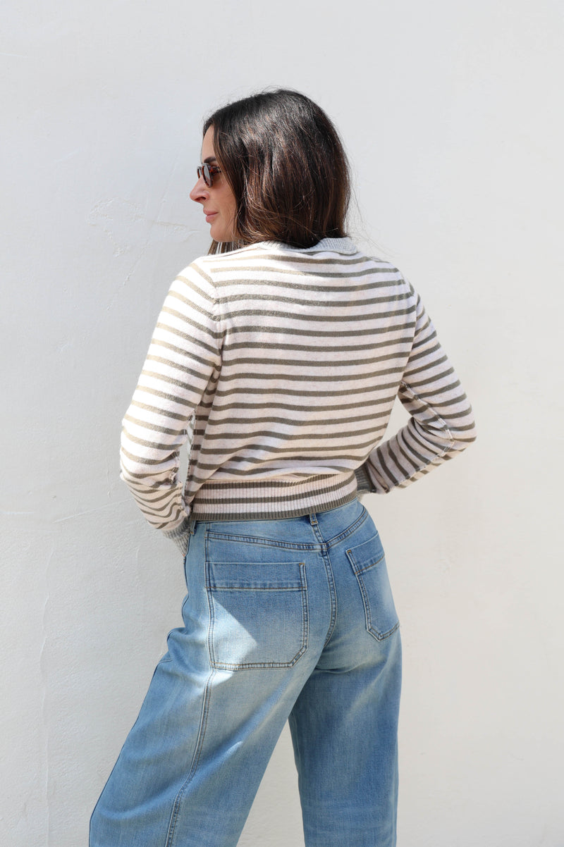 A woman wearing a ribbed knit cardigan with horizontal gray and off-white stripes, paired with blue jeans.
