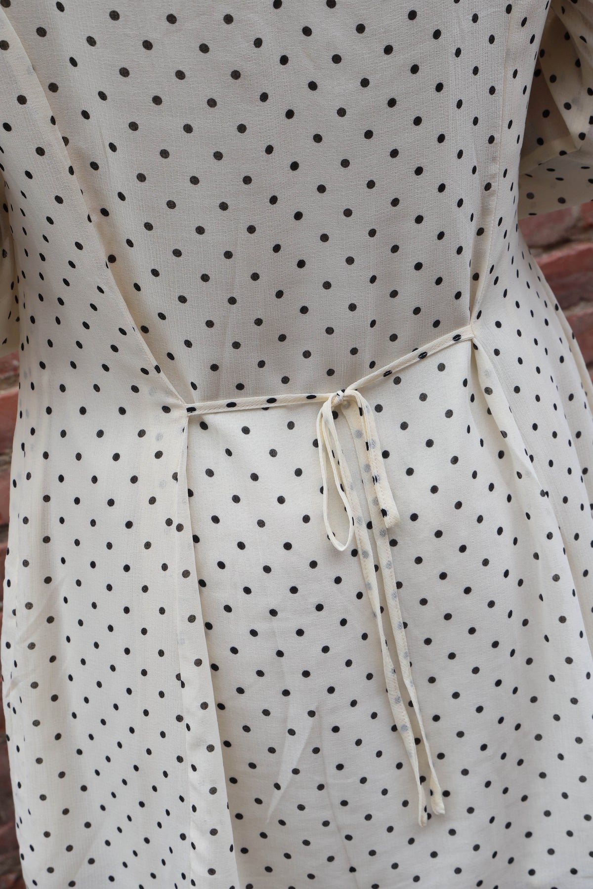 Details of polka dot dress against a brick wall