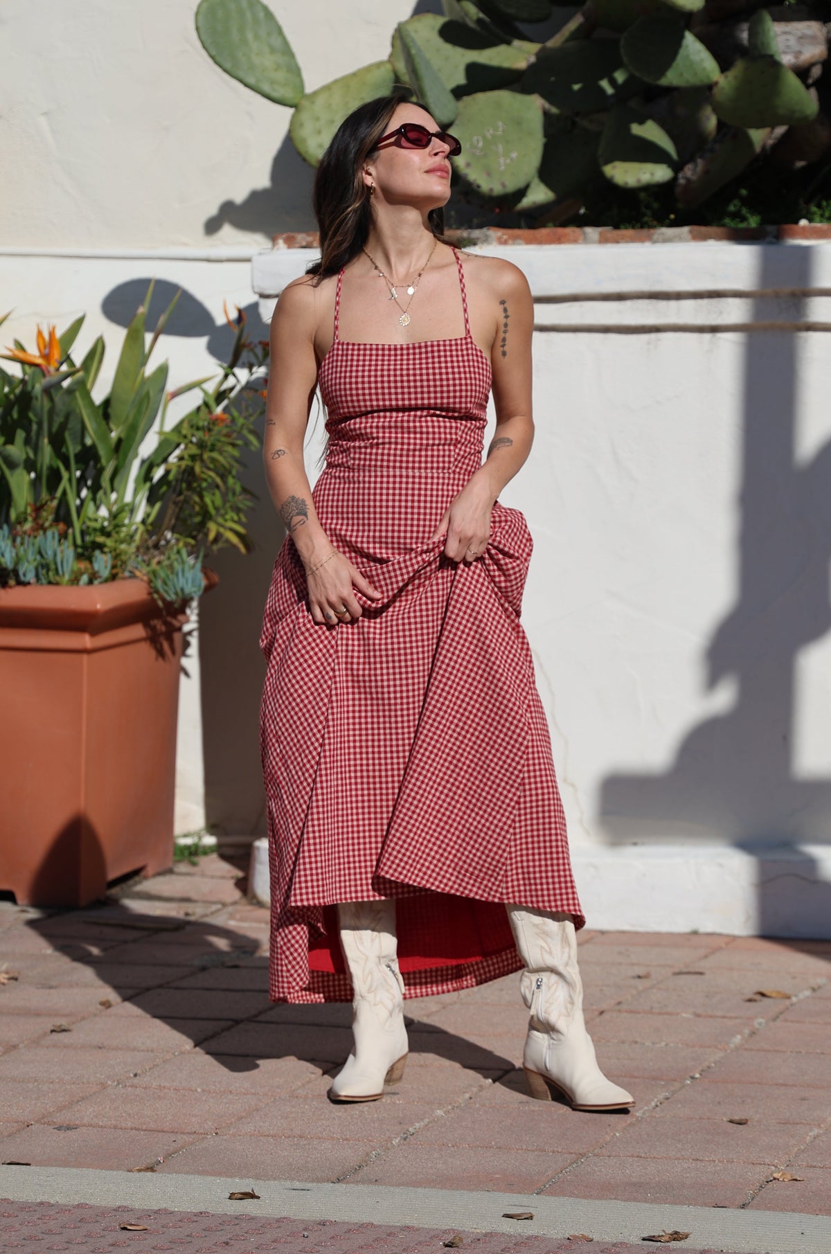 Person wearing a red dress standing on a sidewalk with plants and a cactus nearby.