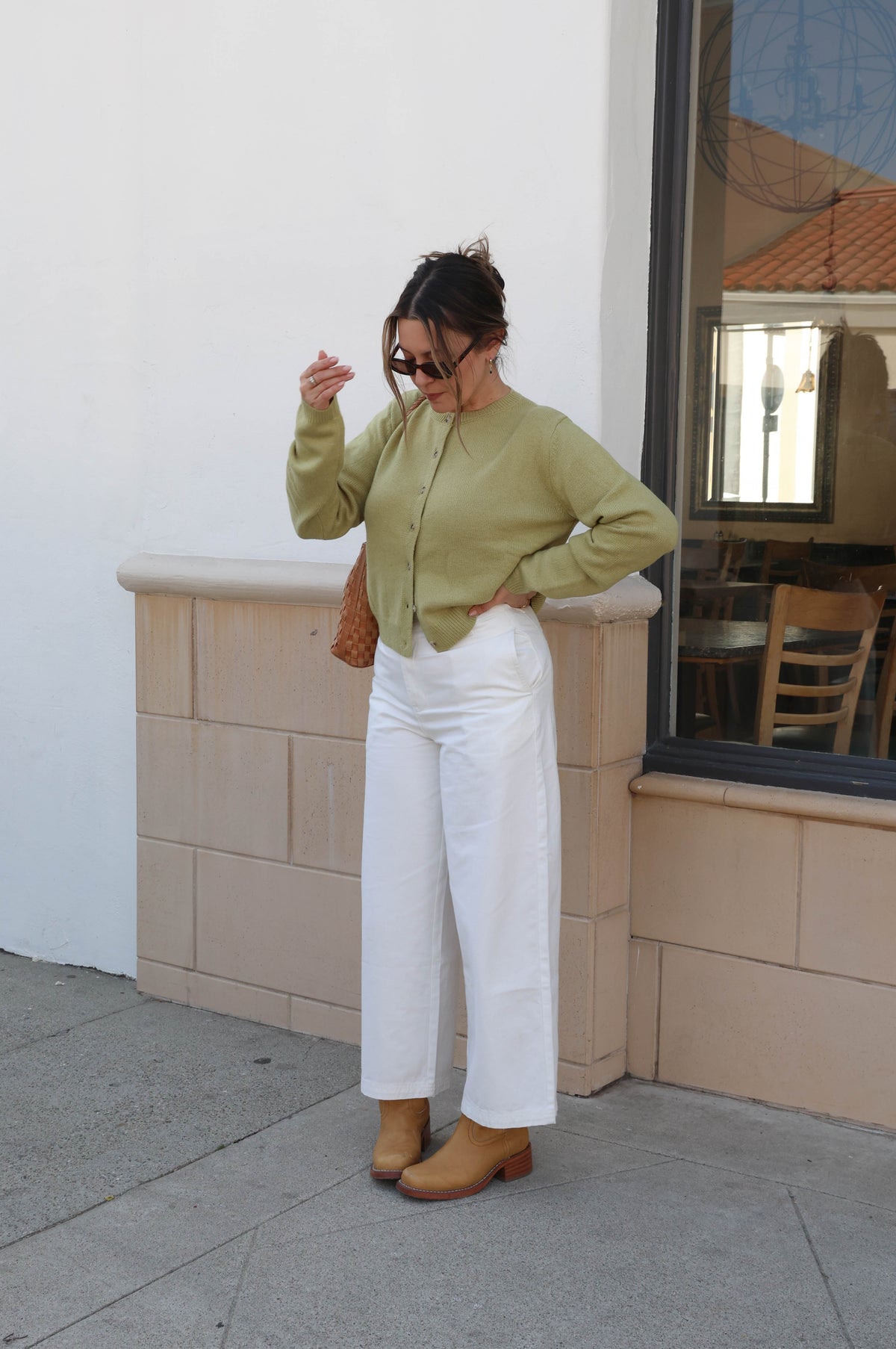 Woman in a green shirt and white pants standing on a sidewalk with a building in the background.