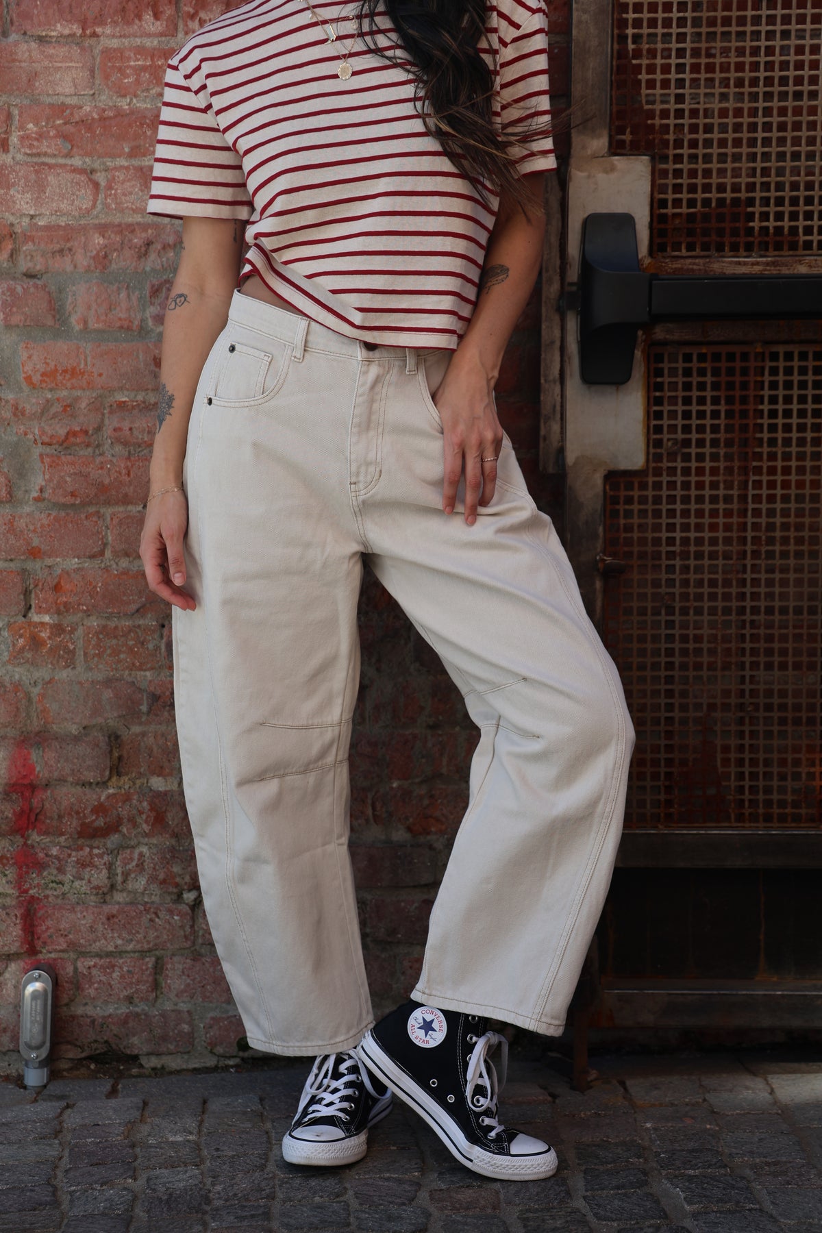 Person wearing white pants and a red and white striped shirt, sitting on a bench against a brick wall.