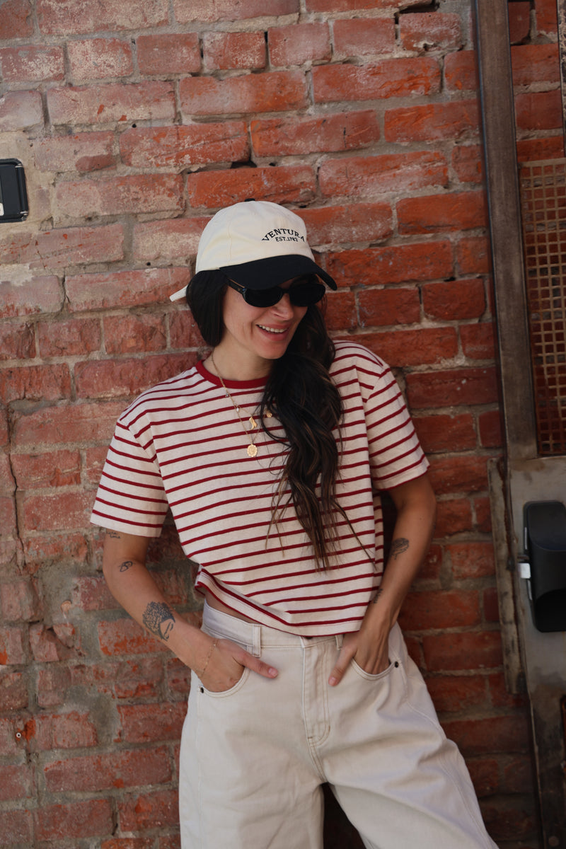 Person wearing a red and white striped shirt and white cap against a brick wall.