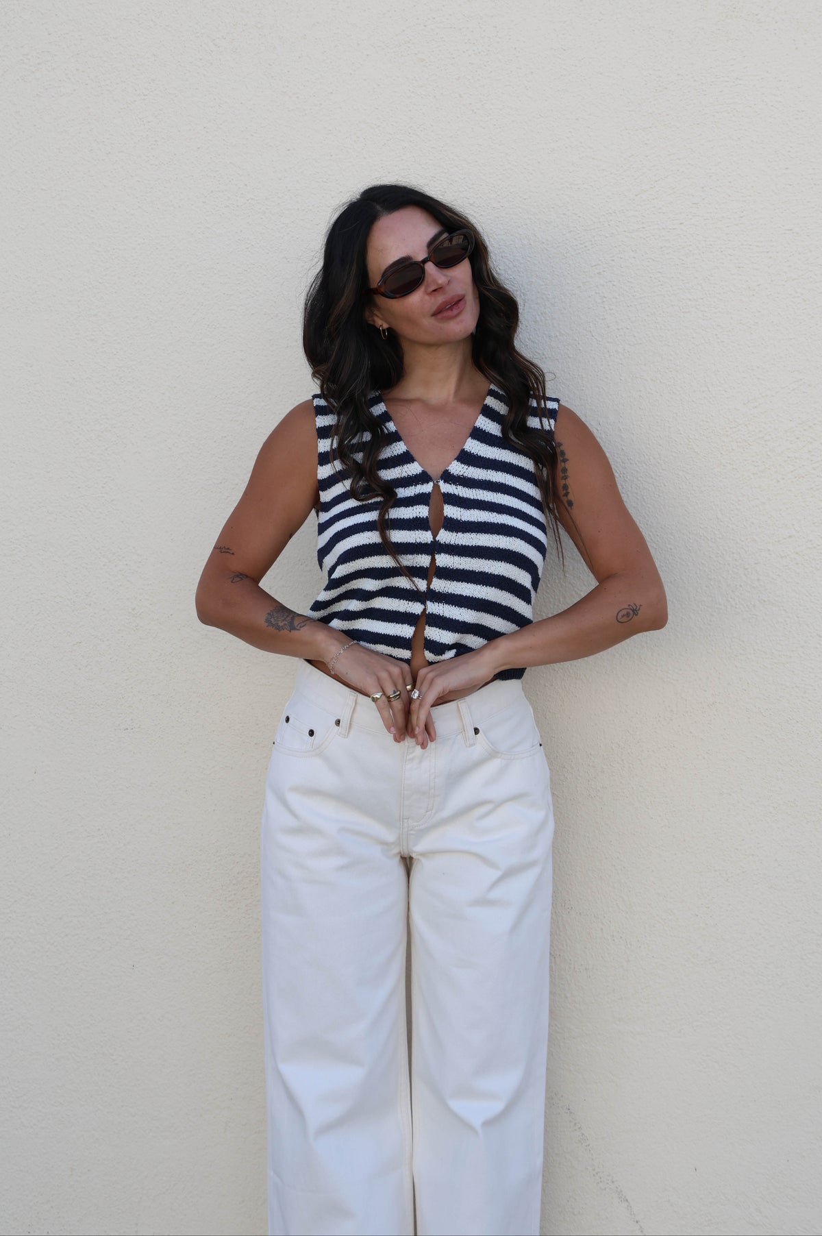 Woman wearing a striped tank with white pants against a white wall