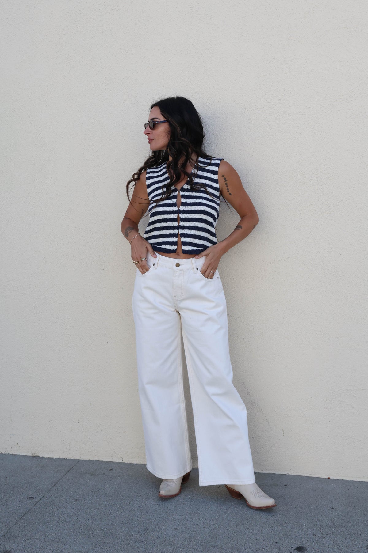 Woman wearing a striped tank with white pants against a white wall