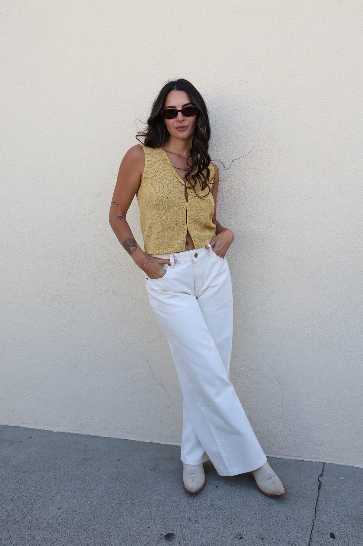 Woman wearing a yellow tank top with white pants against a white wall