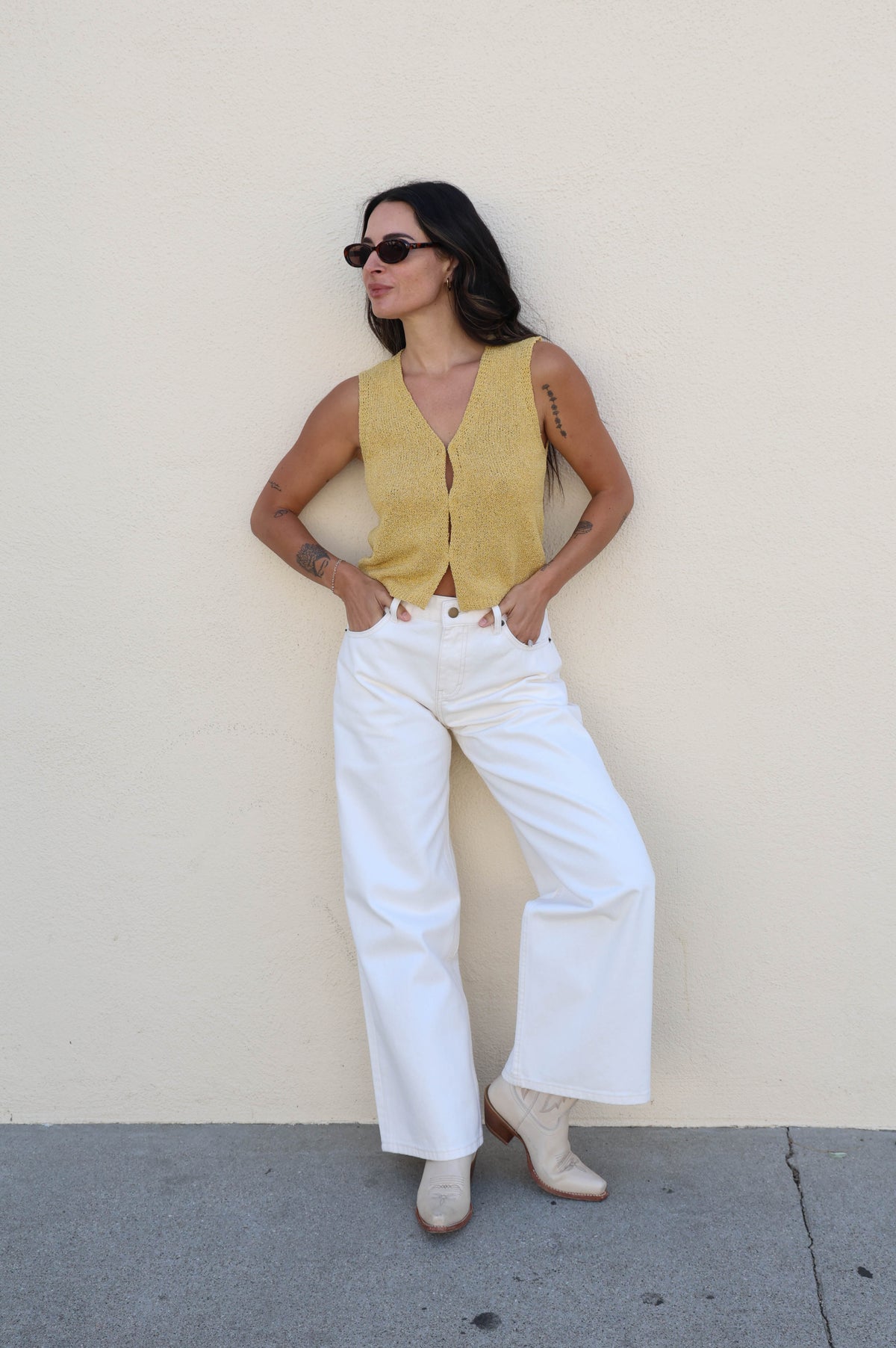 Woman wearing a yellow tank top with white pants against a white wall