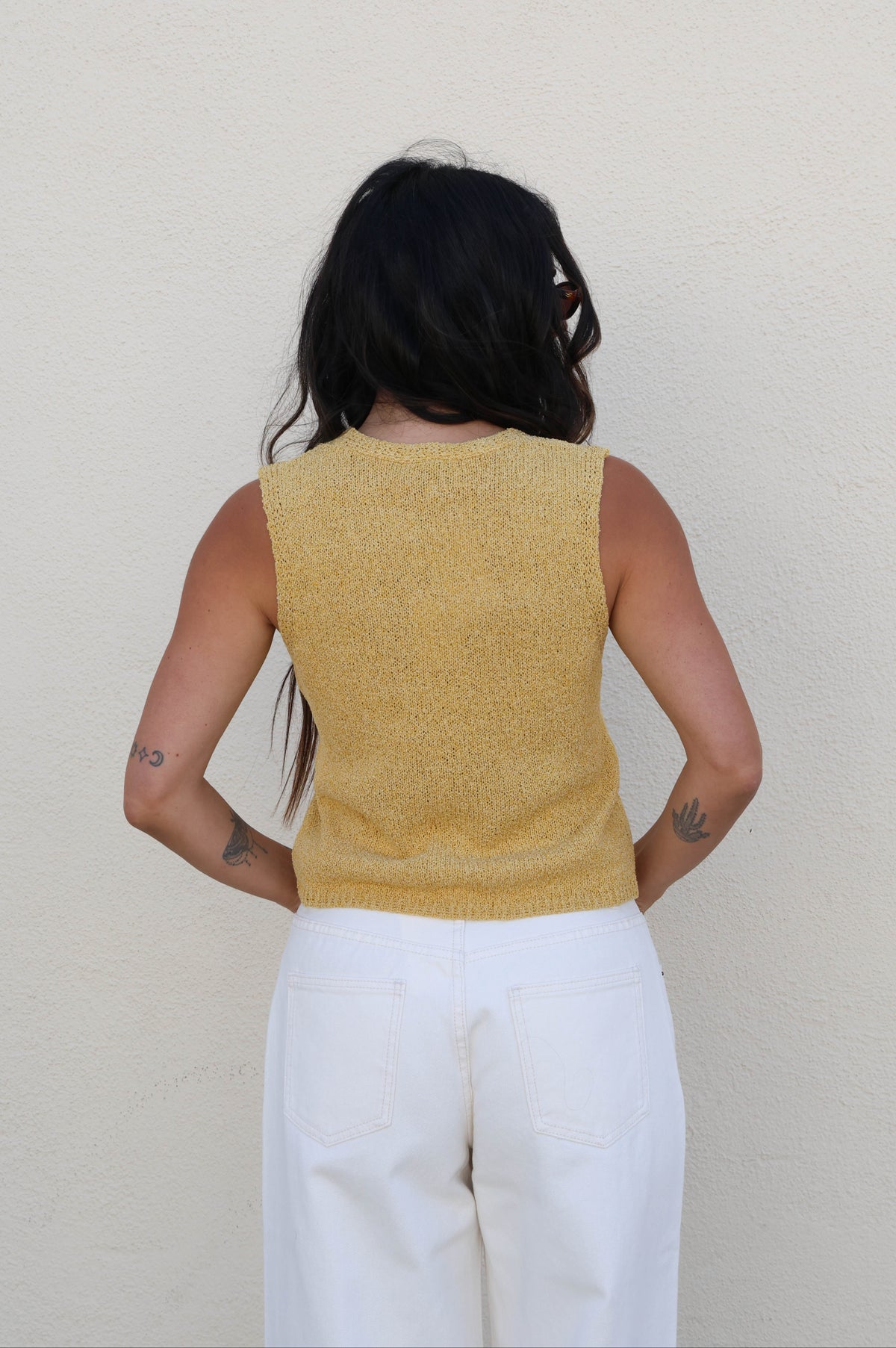 Woman wearing a yellow tank top with white pants against a white wall