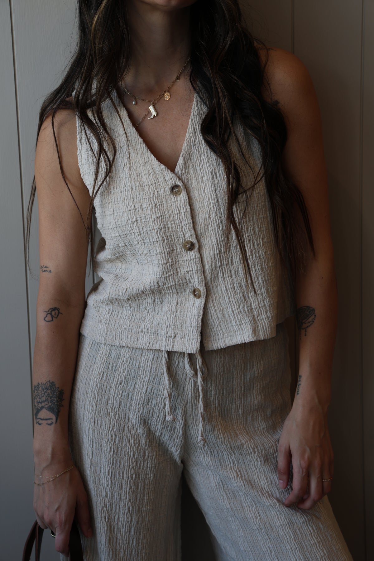Person wearing a light-colored sleeveless top with buttons, lying on a white surface.