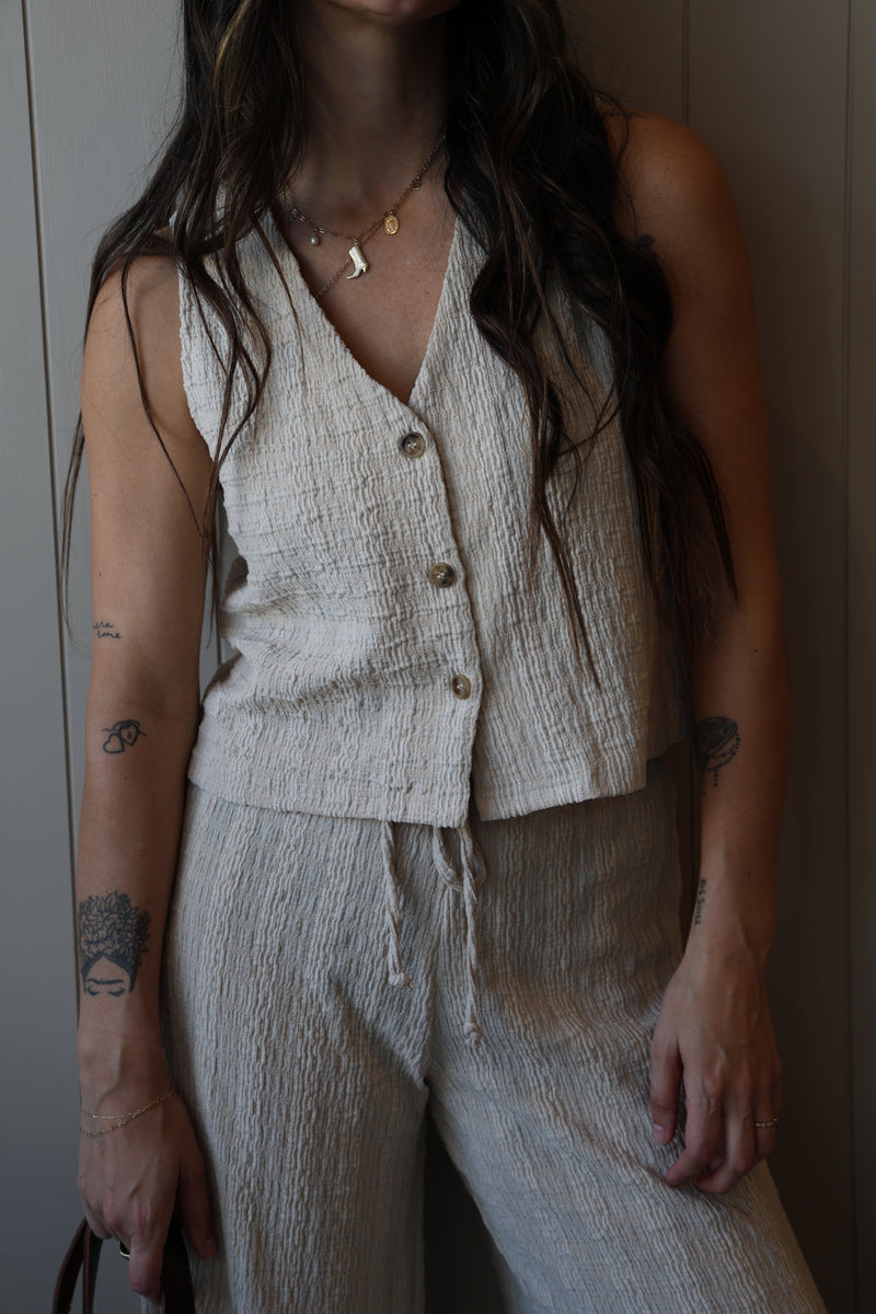 Person wearing a light-colored sleeveless top with buttons, lying on a white surface.