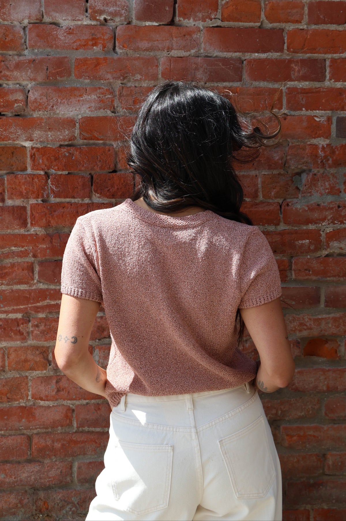 Woman in a pink button up blouse with with jeans against a brick wall