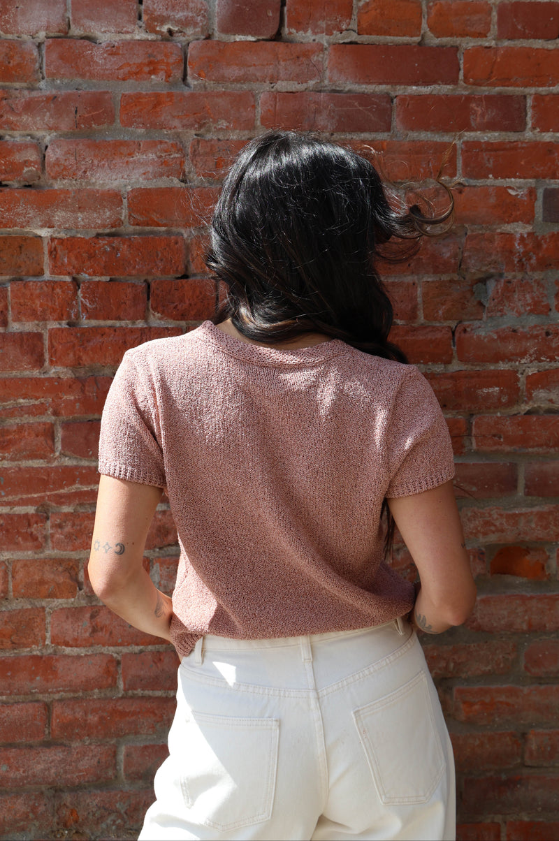 Woman in a pink button up blouse with with jeans against a brick wall
