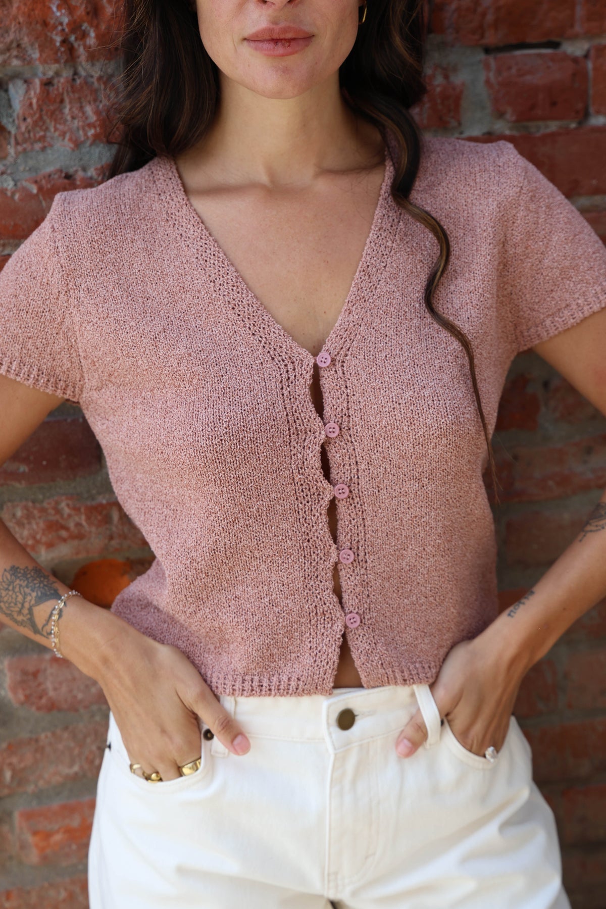 Woman in a pink button up blouse with with jeans against a brick wall