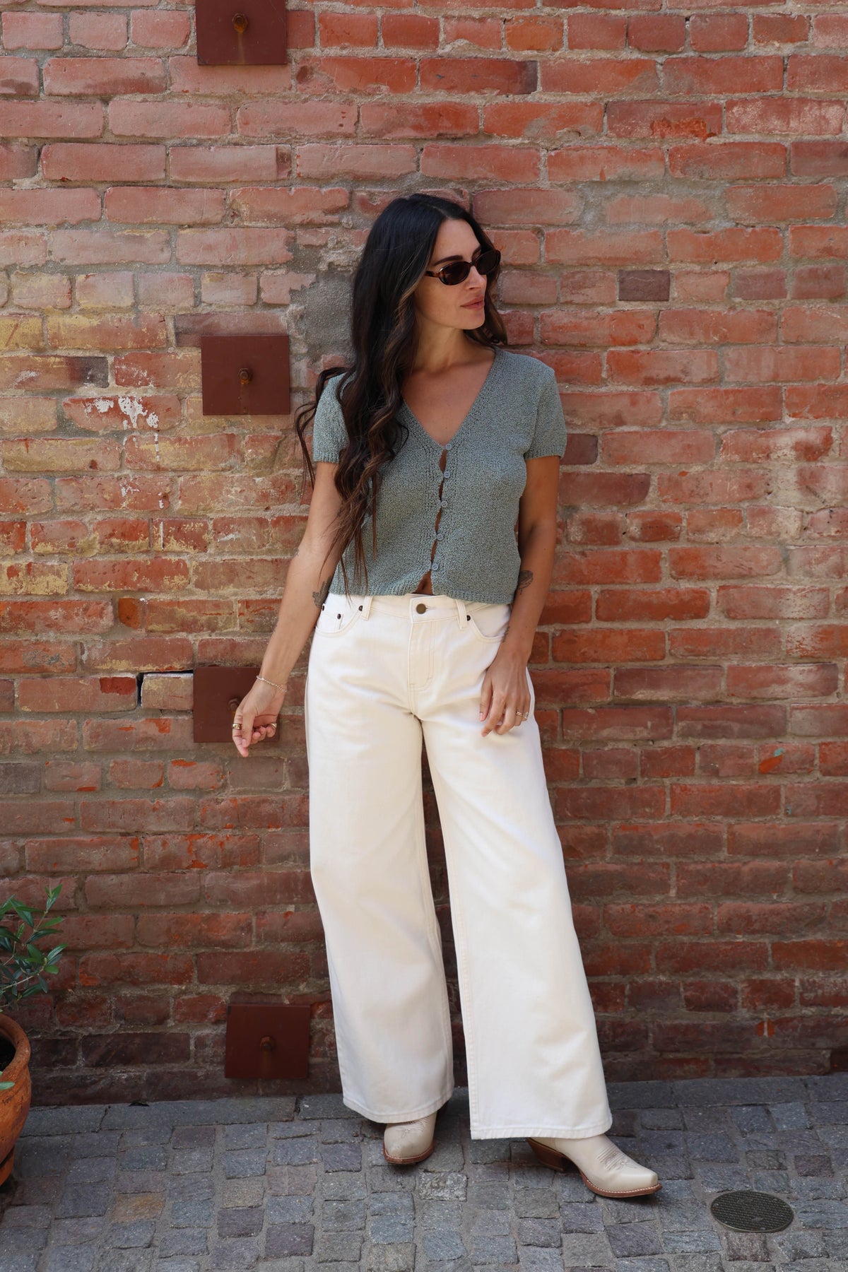 Woman in a teal button up blouse with with jeans against a brick wall