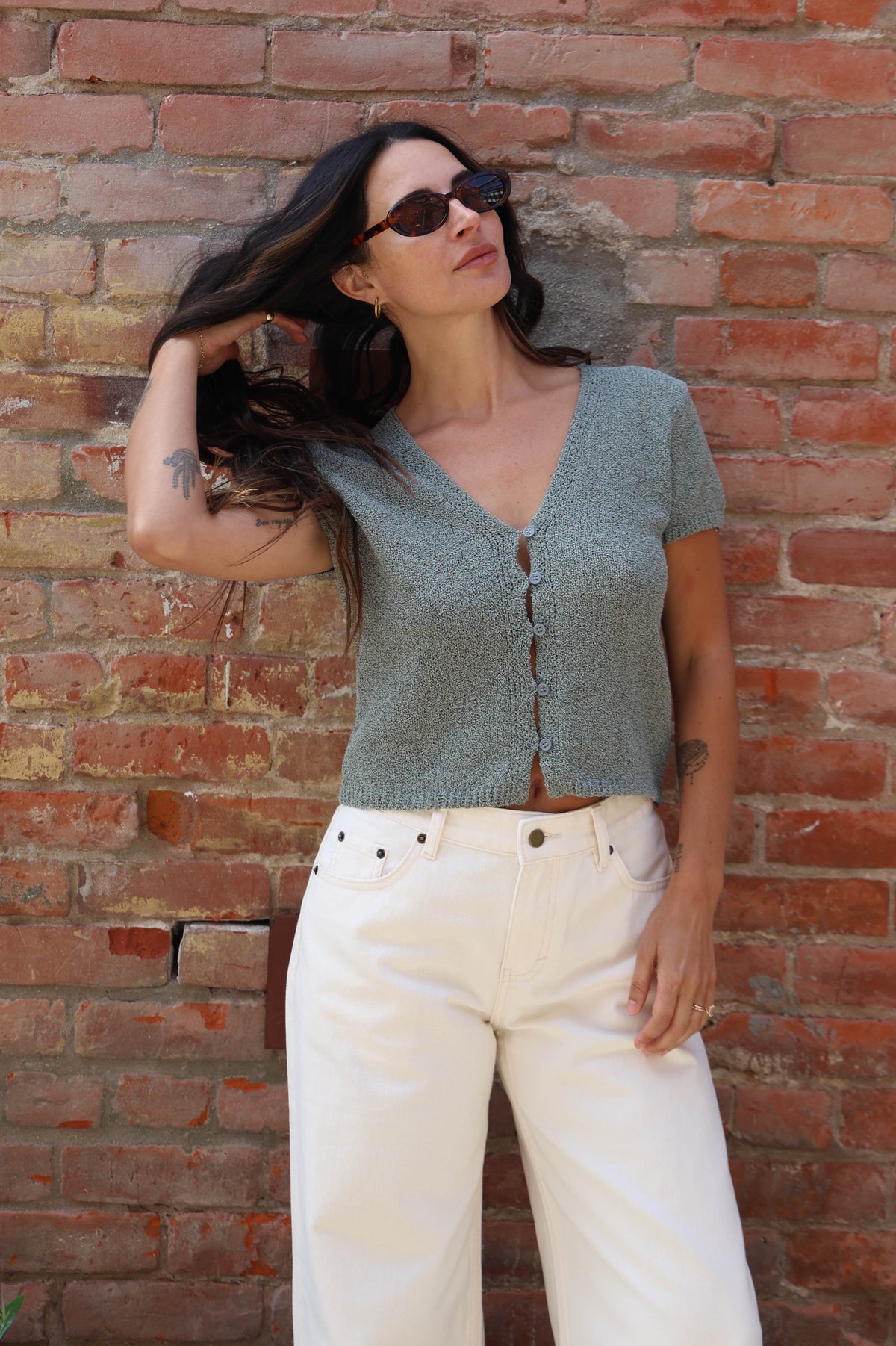 Woman in a teal button up blouse with with jeans against a brick wall