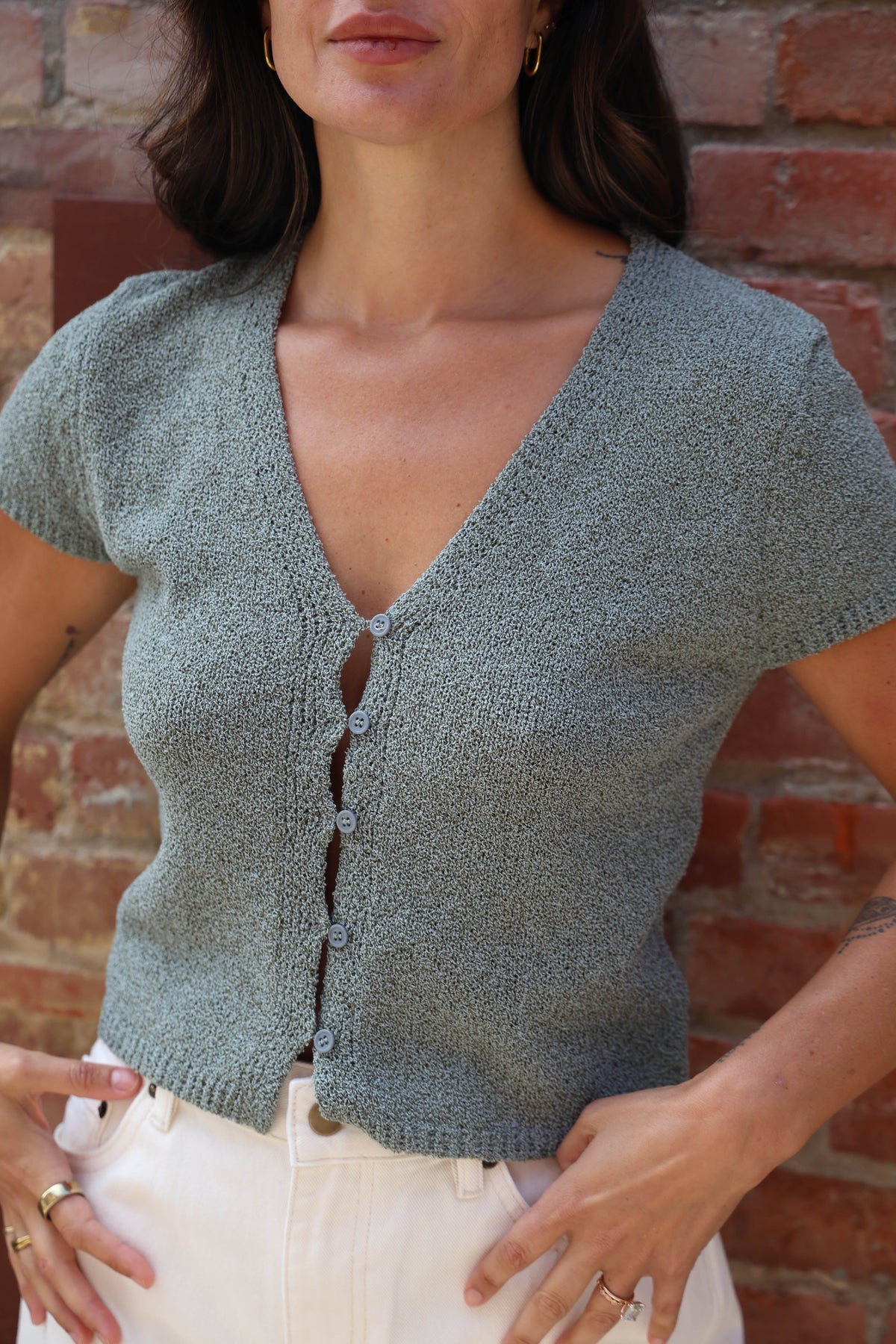 Woman in a teal button up blouse with with jeans against a brick wall