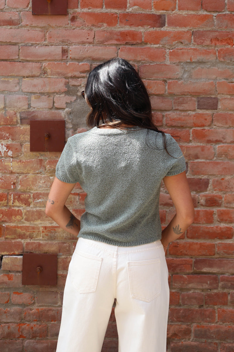 Woman in a teal blouse with with jeans against a brick wall