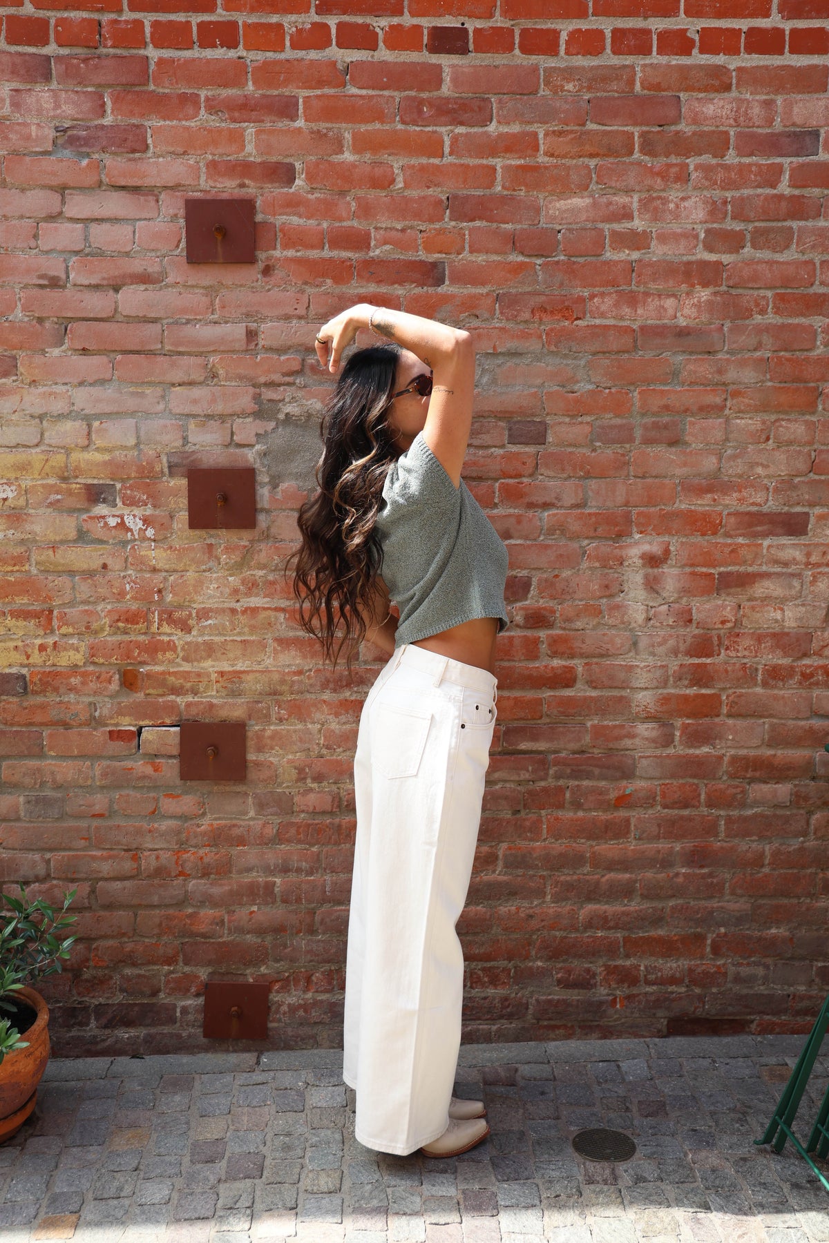 Woman in a teal button up blouse with with jeans against a brick wall
