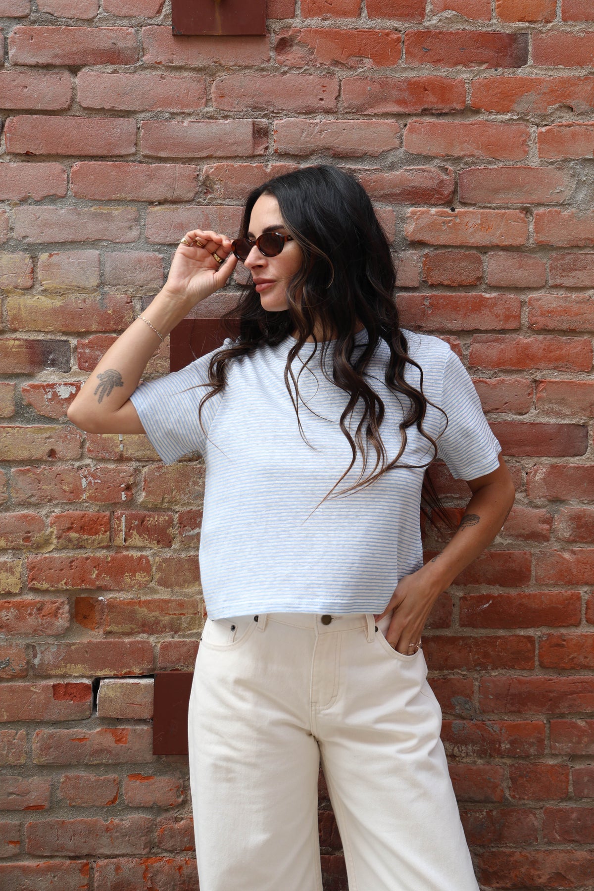 Woman wearing a white and blue striped top and beige pants against a brick wall