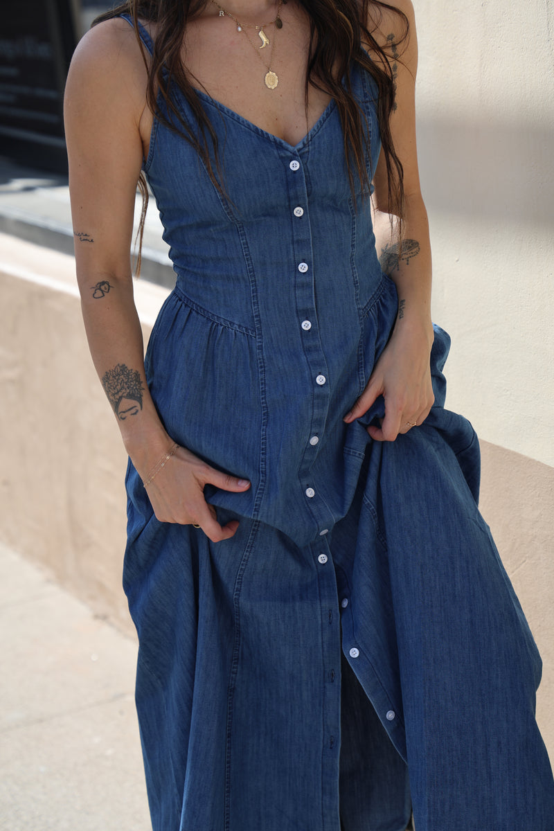 Woman wearing a blue dress with white buttons, standing against a neutral background