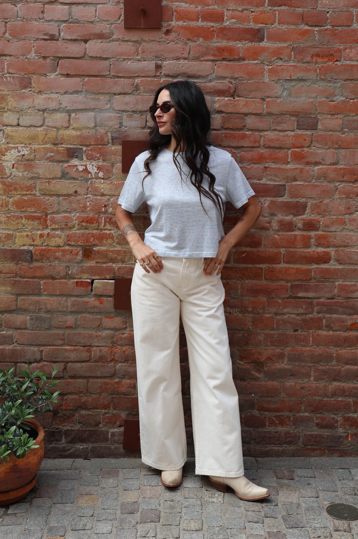 Person wearing a light blue t-shirt and white pants standing against a brick wall.