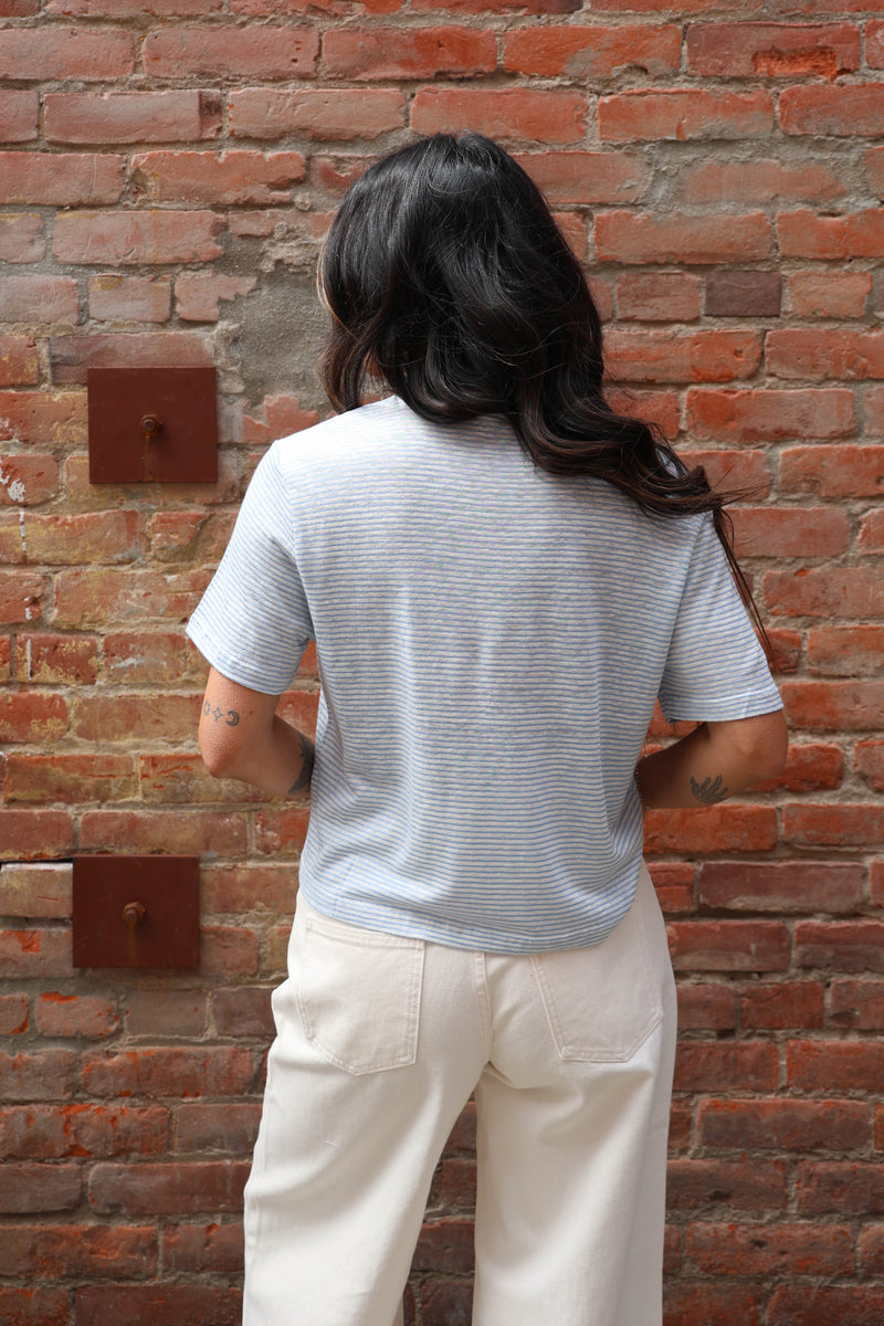Person wearing a striped shirt and light-colored pants against a brick wall.