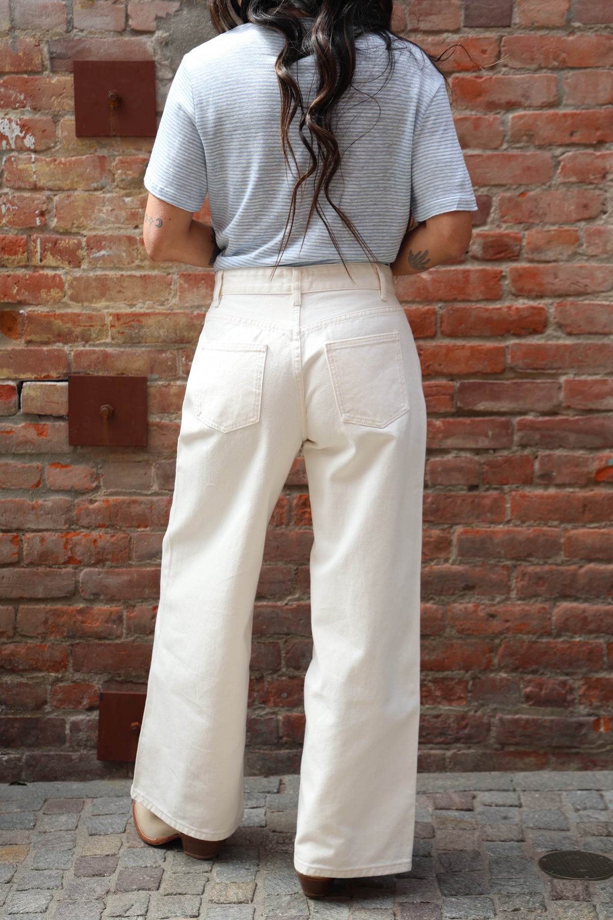Person wearing a light gray t-shirt and white pants standing against a brick wall.