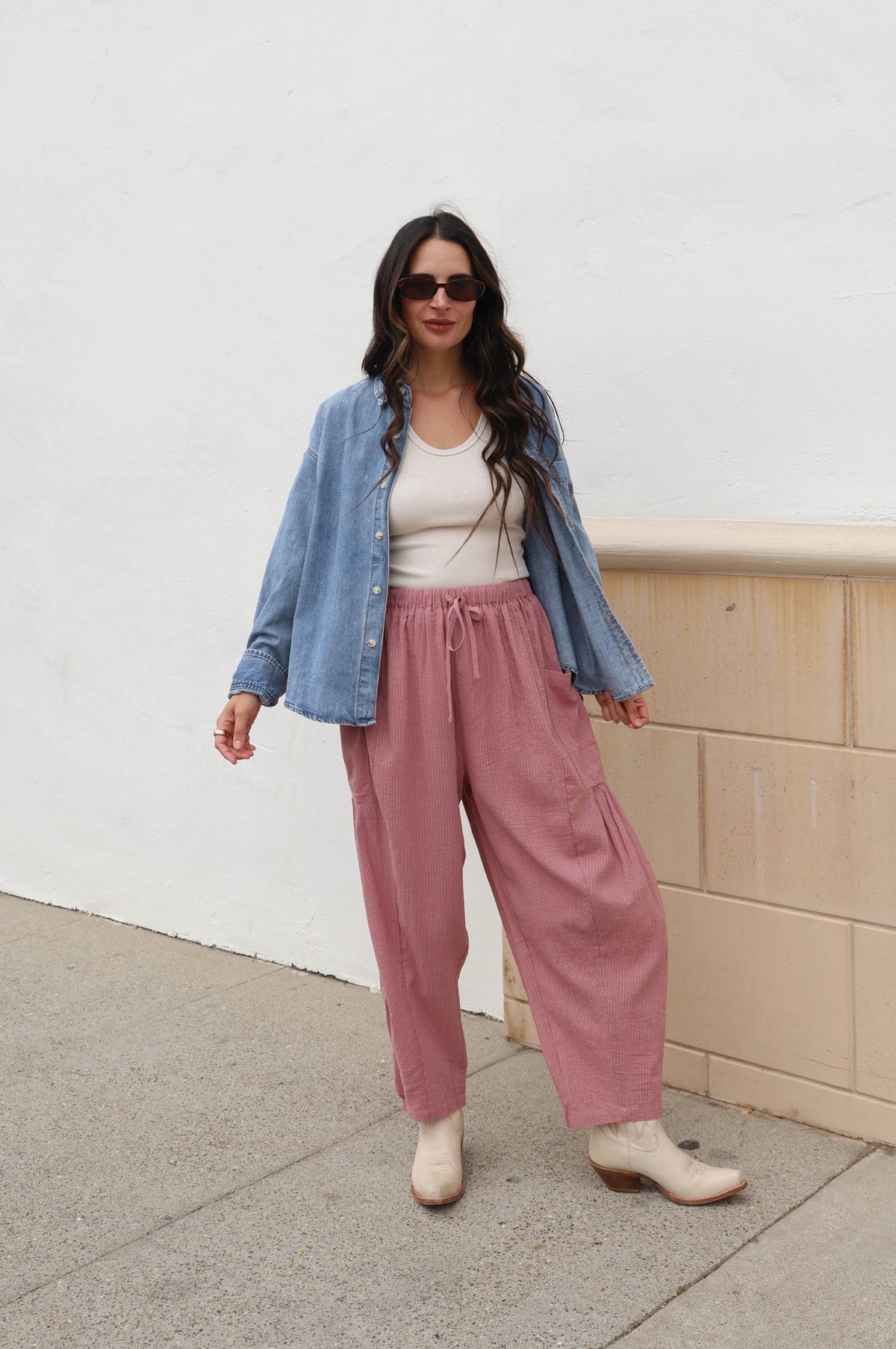 Woman wearing a jean shacked with pink pants against a white wall