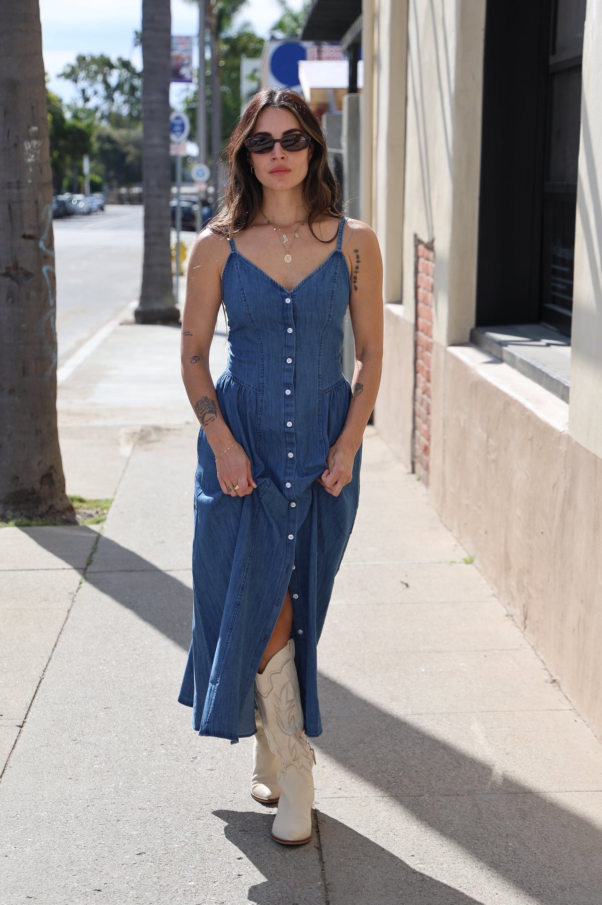 Woman in a blue dress standing on a sidewalk with a building in the background