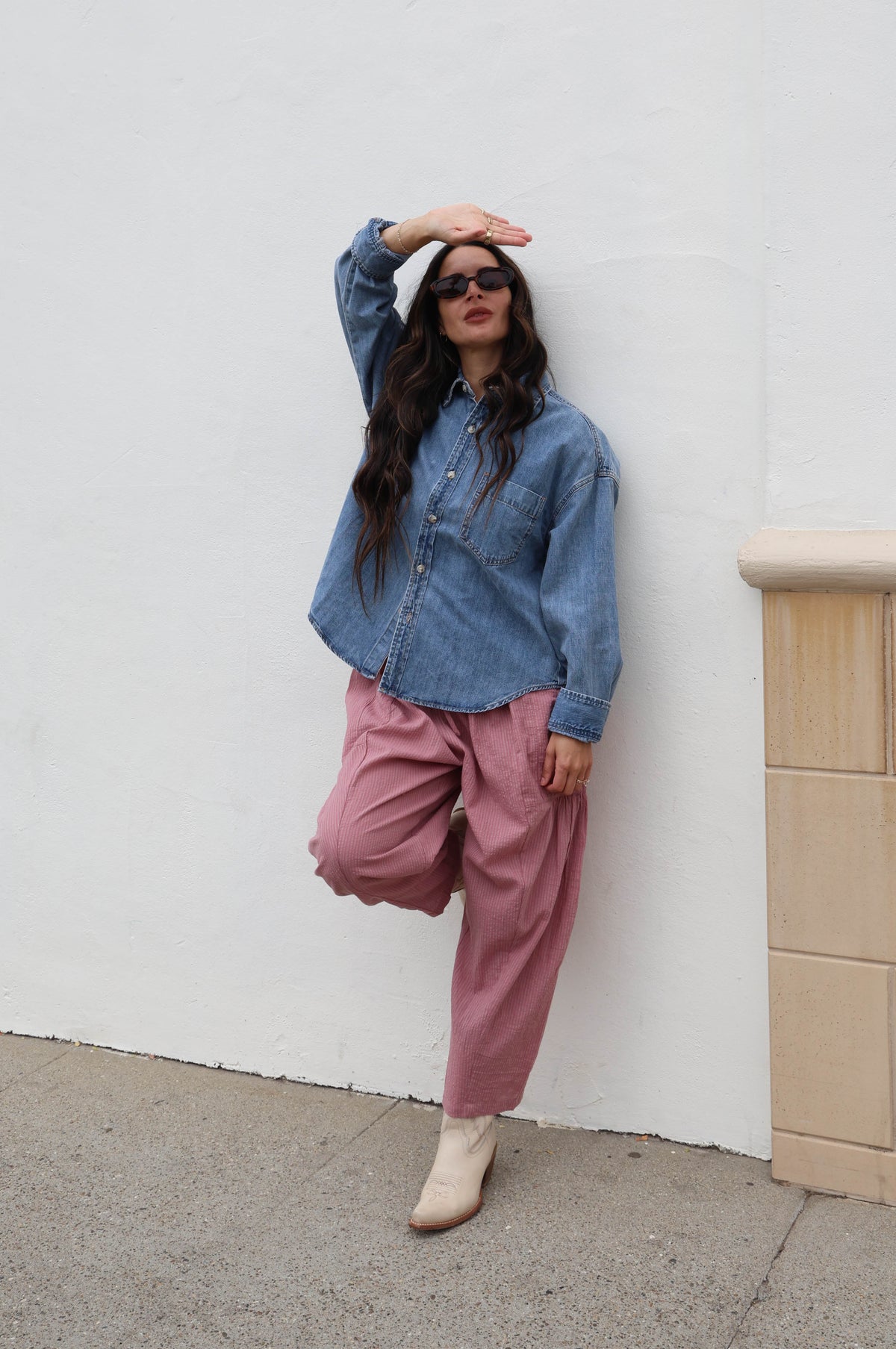Woman wearing a jean shacked with pink pants against a white wall