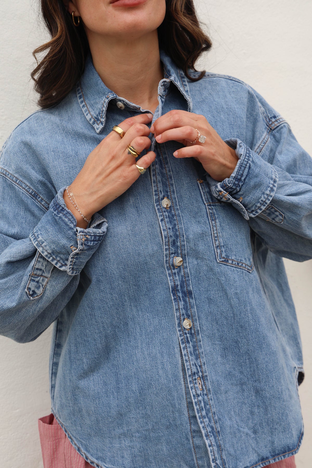 Woman wearing a jean shacked with pink pants against a white wall