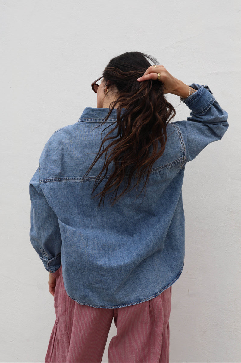 Woman wearing a jean shacked with pink pants against a white wall