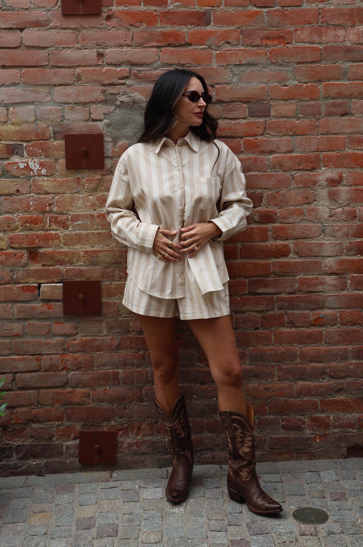 Woman in a striped beige set with cowboy boots against a brick wall