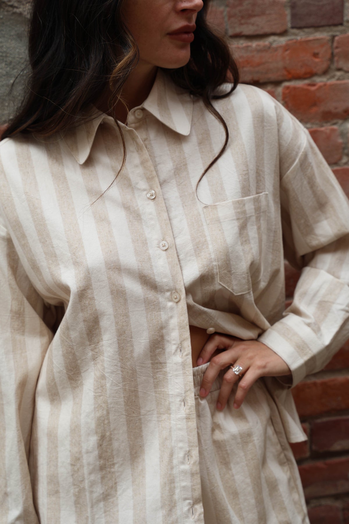 Woman in a striped beige set against a brick wall