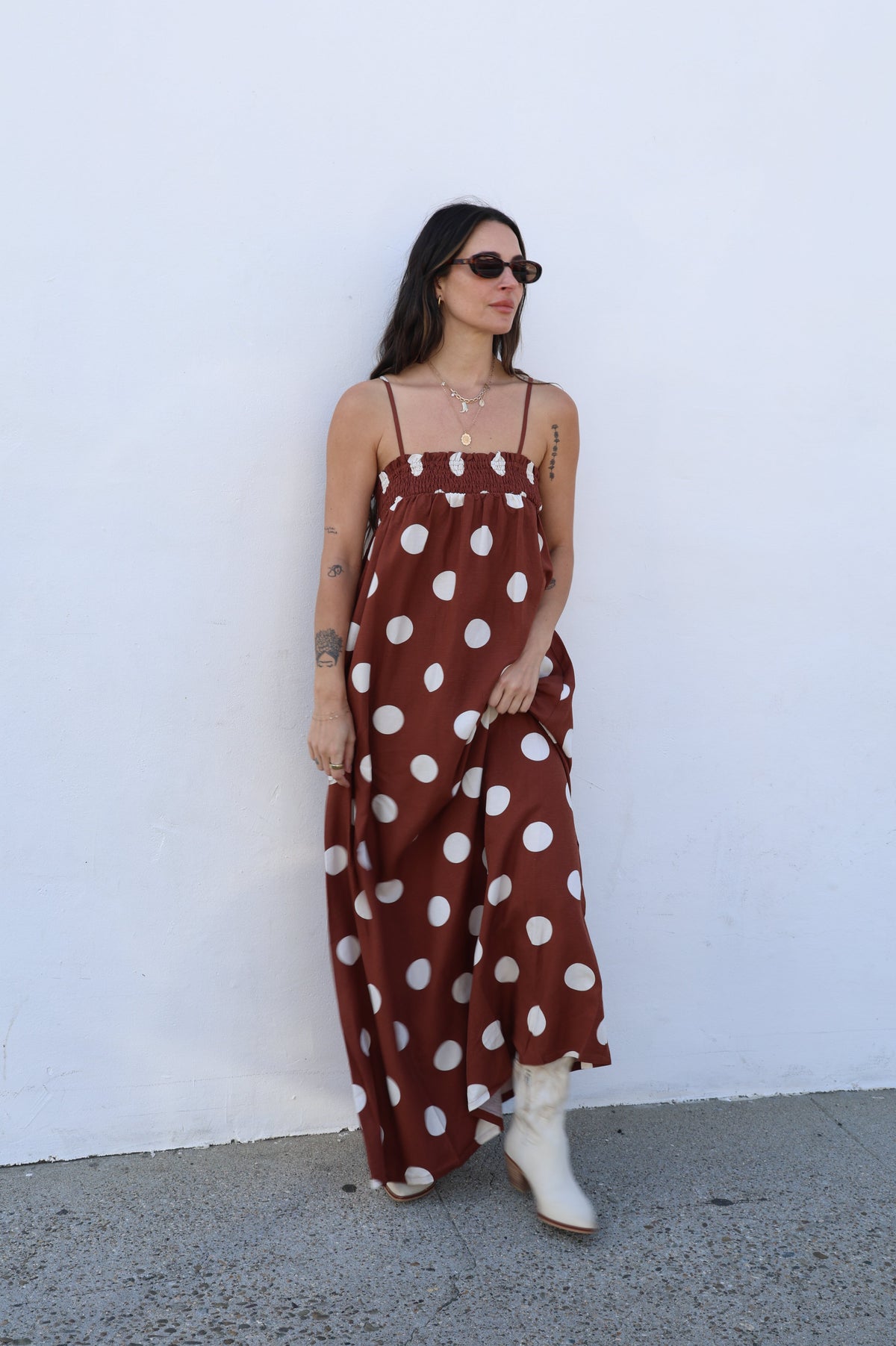 Woman wearing a brown dress with white polka dots against a white wall.