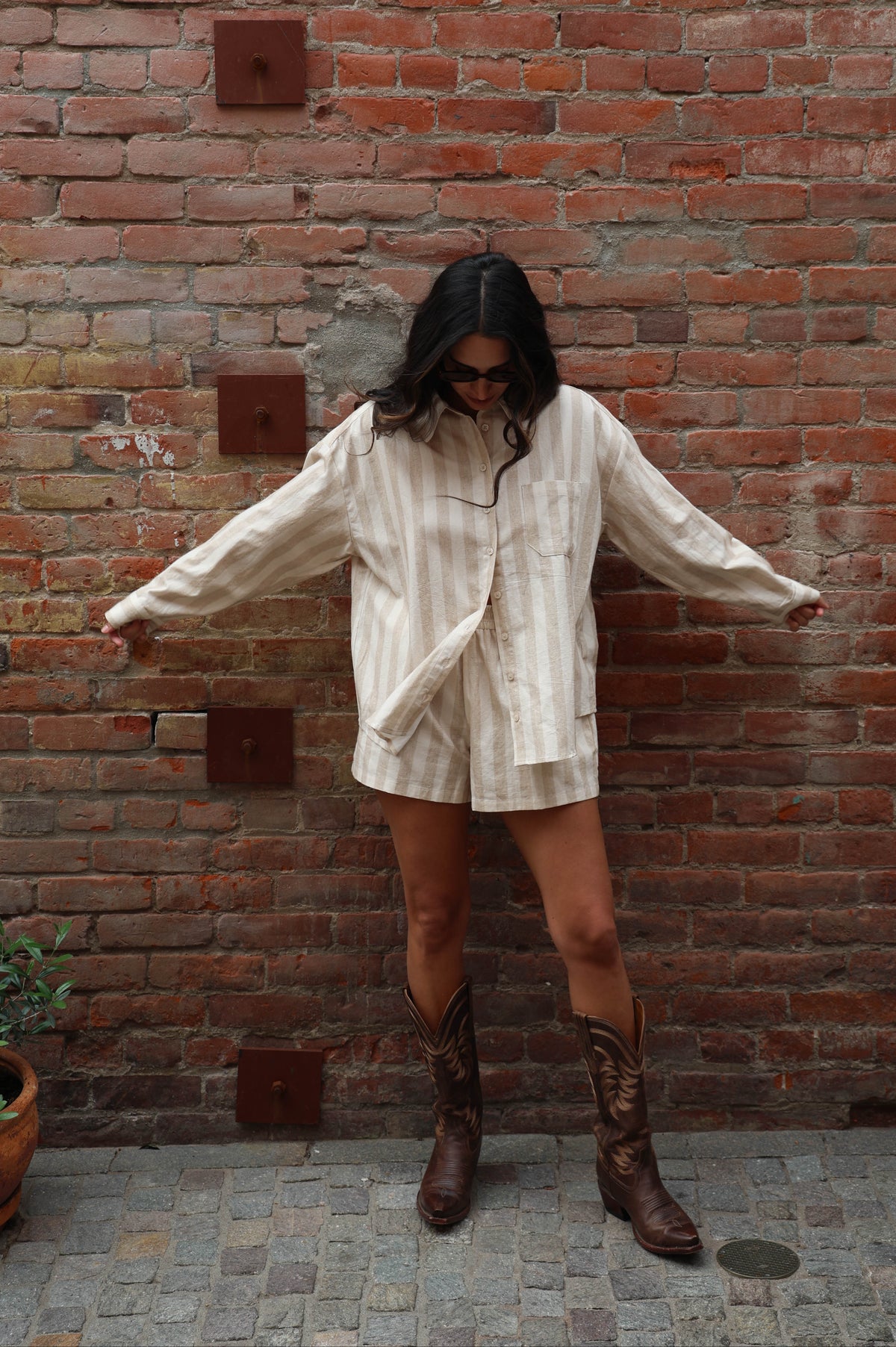 Woman in a striped beige set with cowboy boots against a brick wall