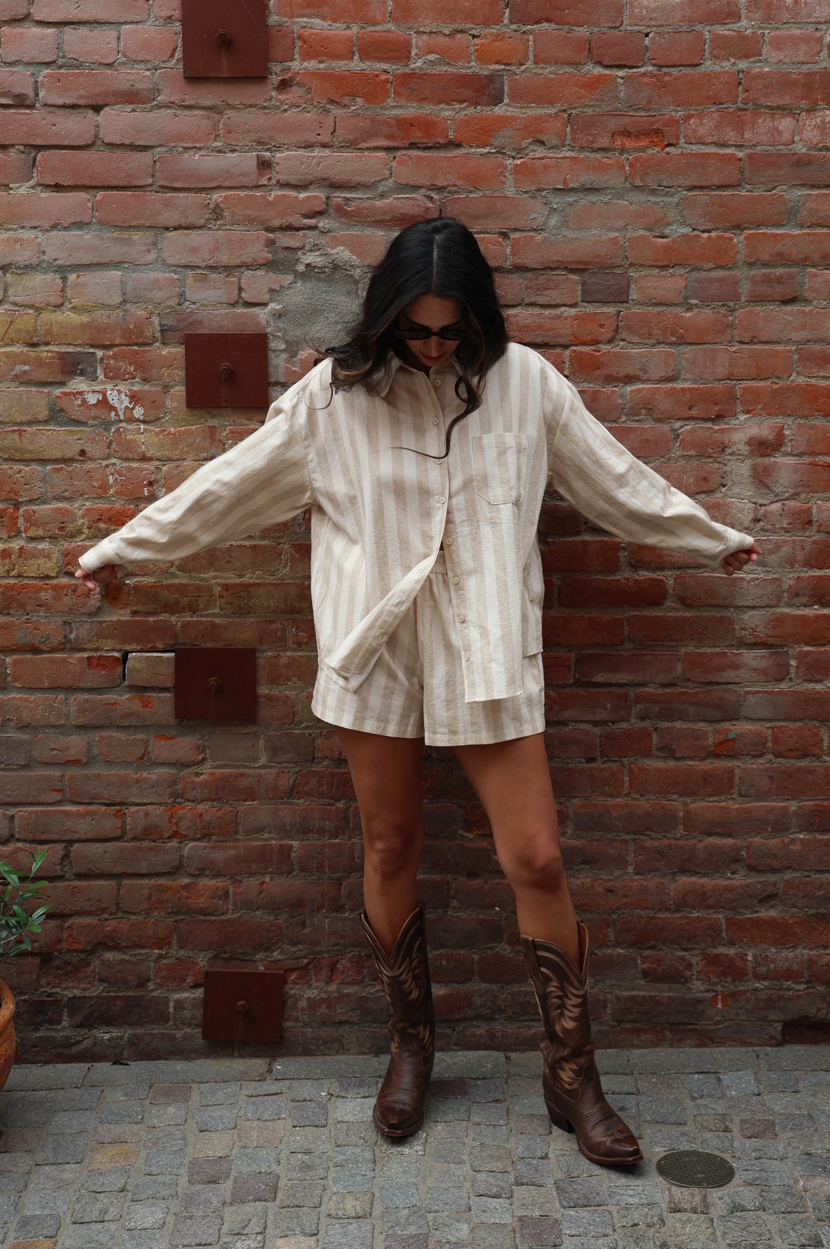 Woman wearing a beige striped set against a brick wall