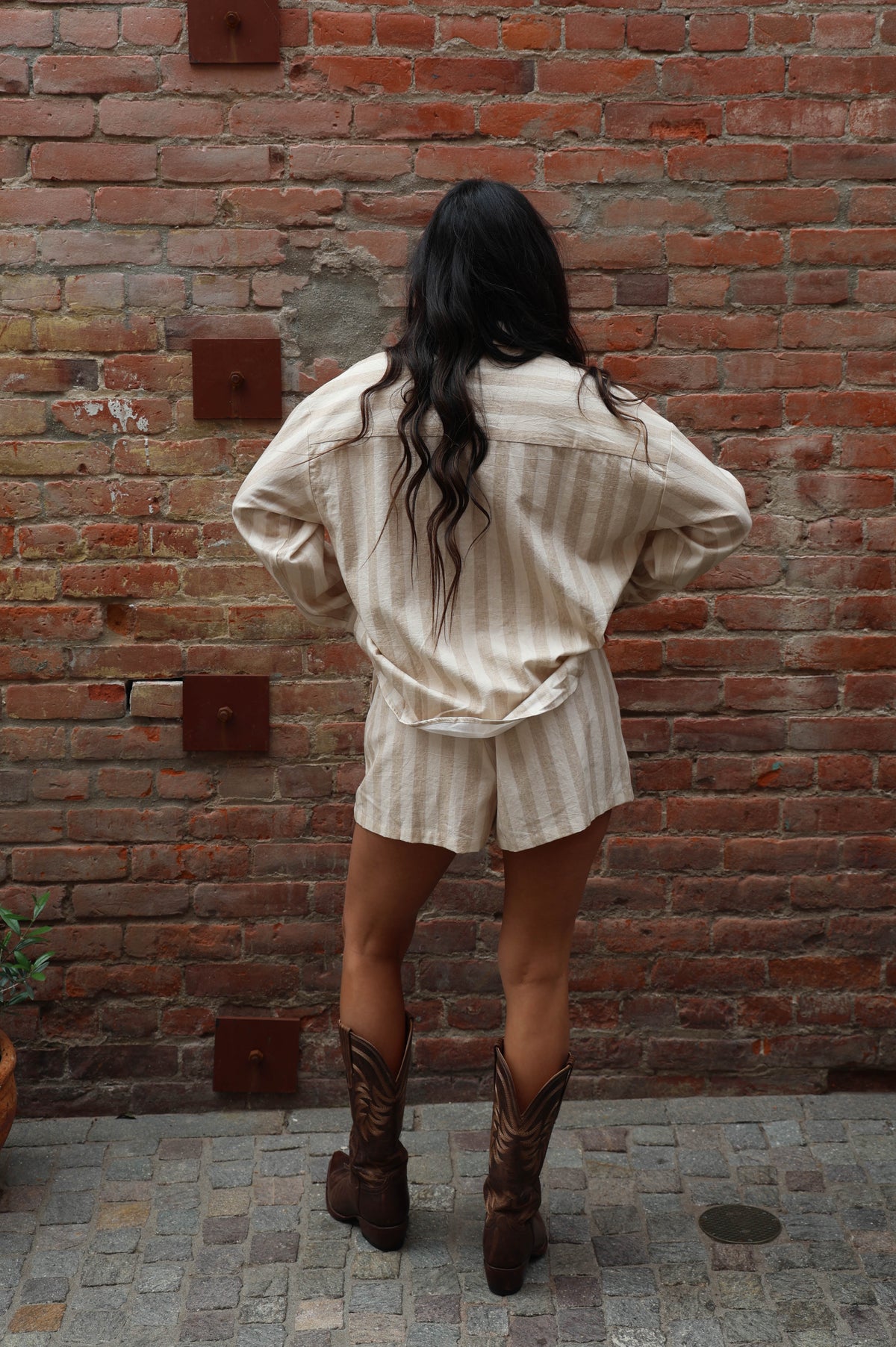 Woman in a striped beige set with cowboy boots against a brick wall