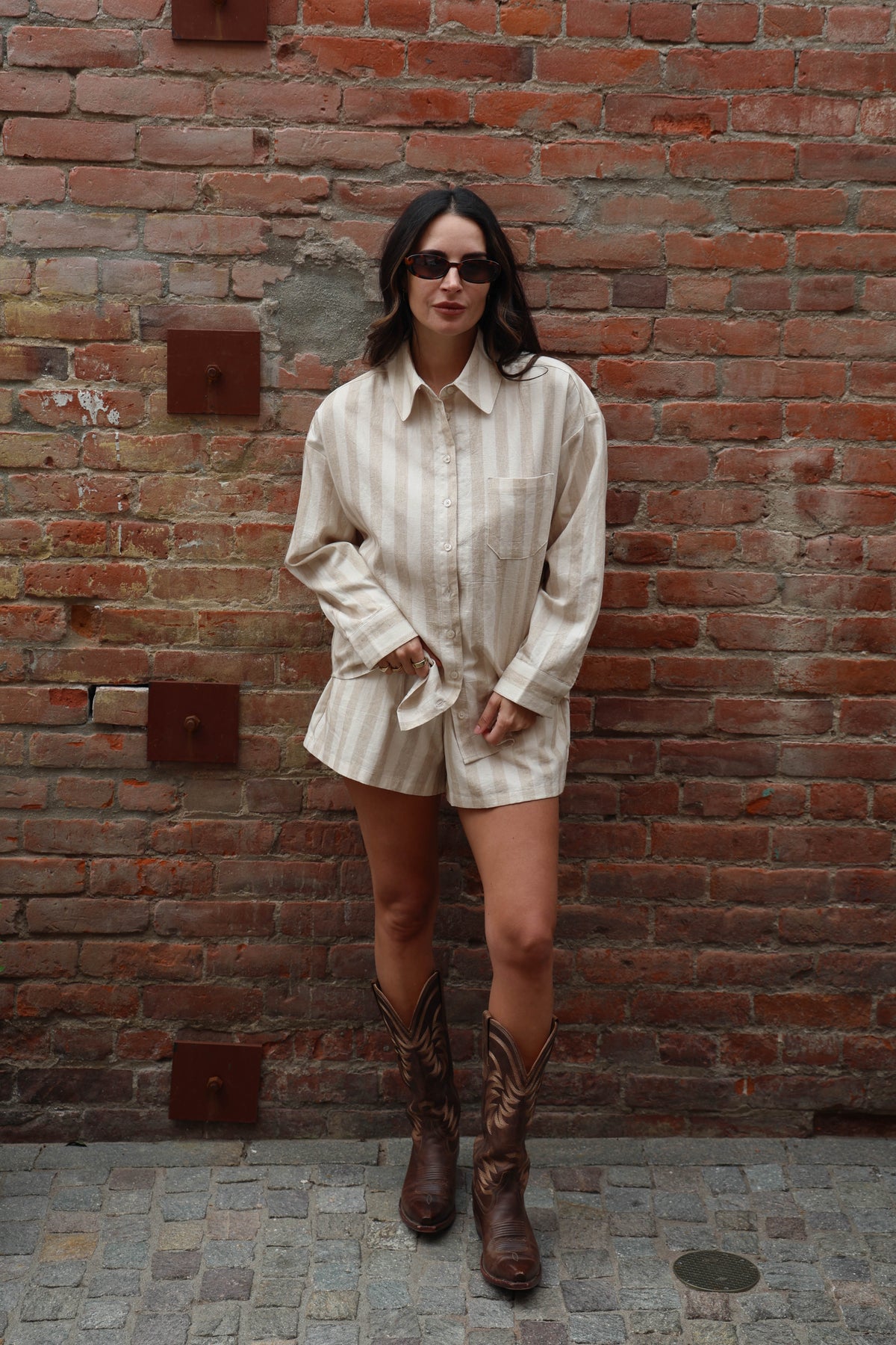 Woman wearing a beige striped set against a brick wall