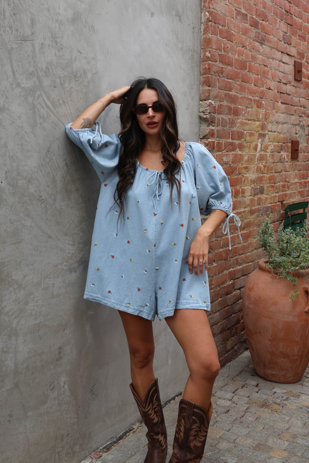 Woman wearing a jean romper with details against grey and brick background