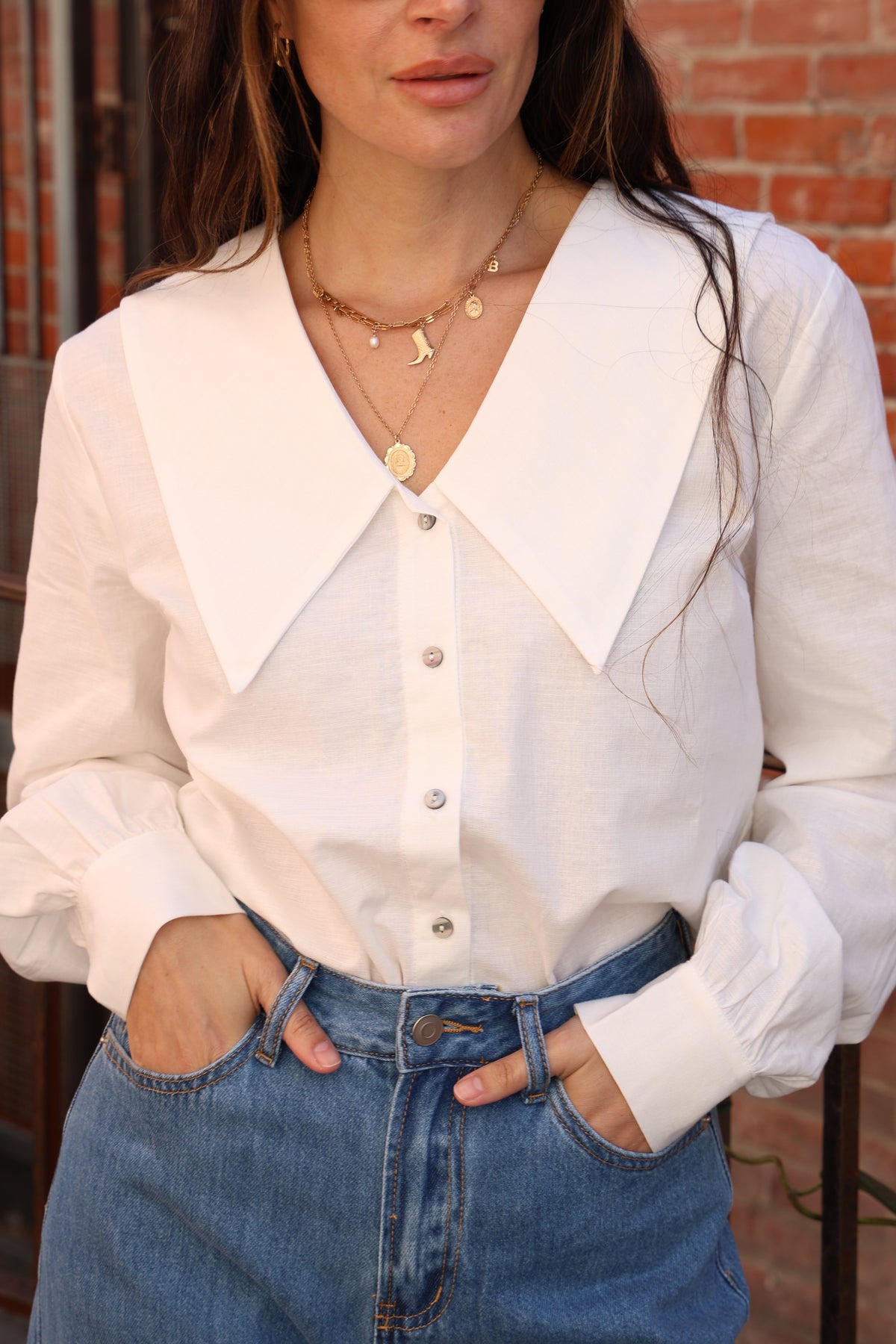 Woman wearing a white blouse and blue jeans with a brick wall background