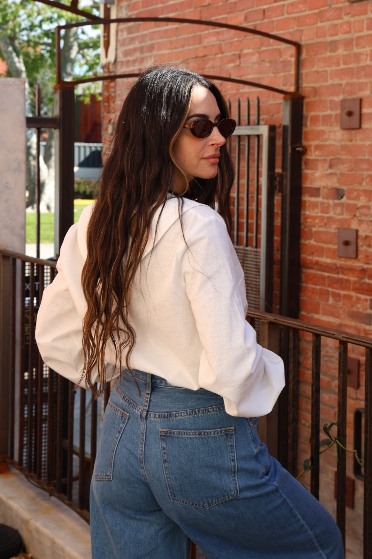 Woman in a white blouse and blue jeans standing in front of a brick wall.