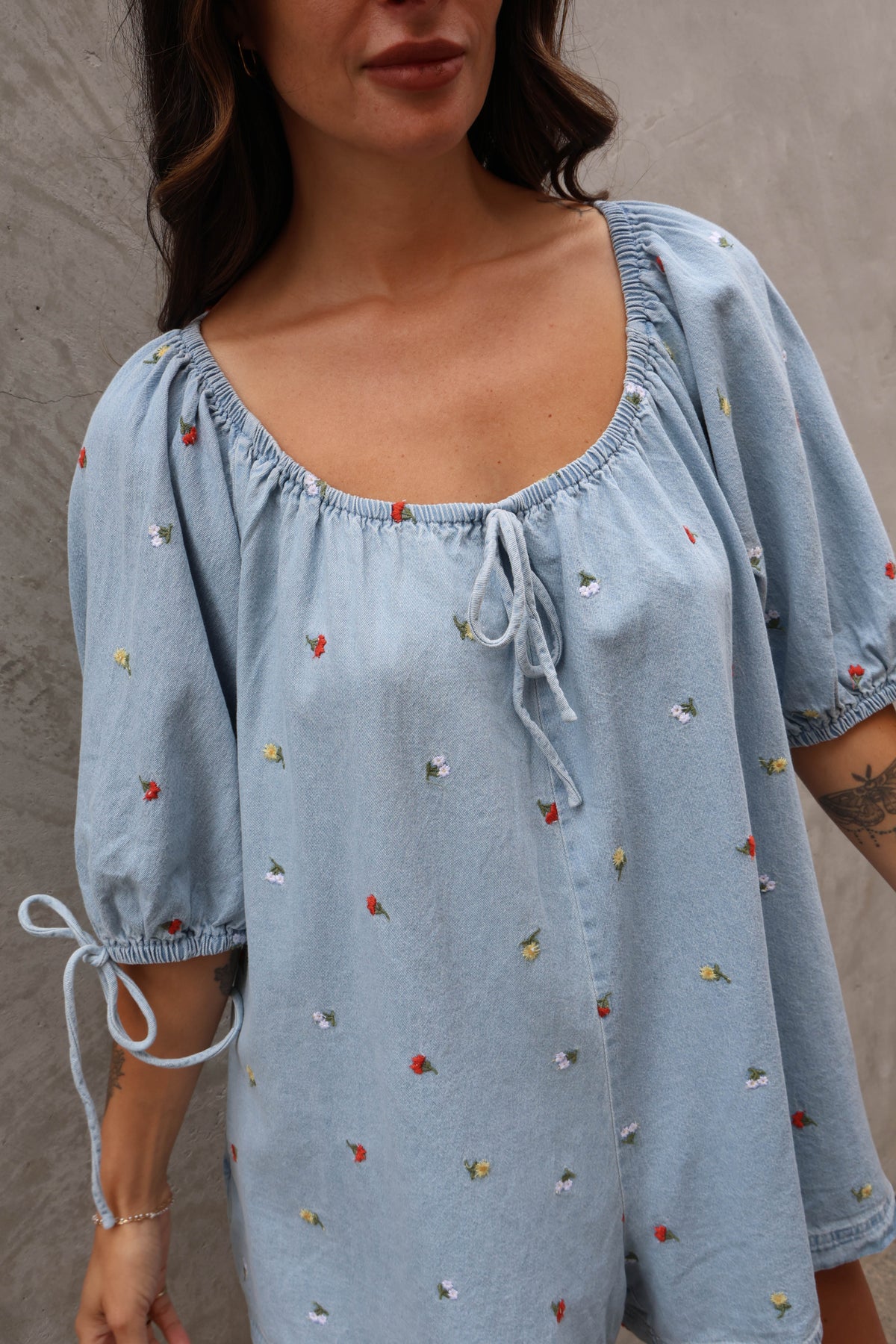 Woman wearing a jean romper with details against a grey background