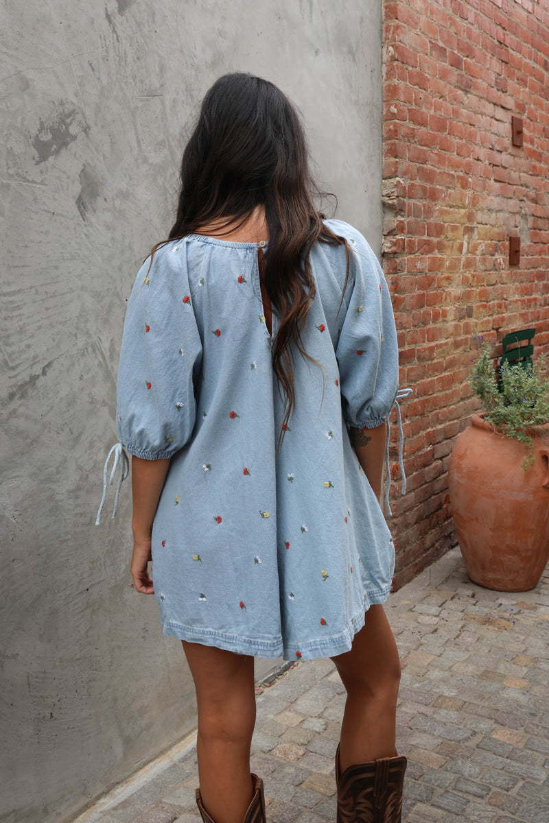 Woman wearing a jean romper with details against grey and brick background