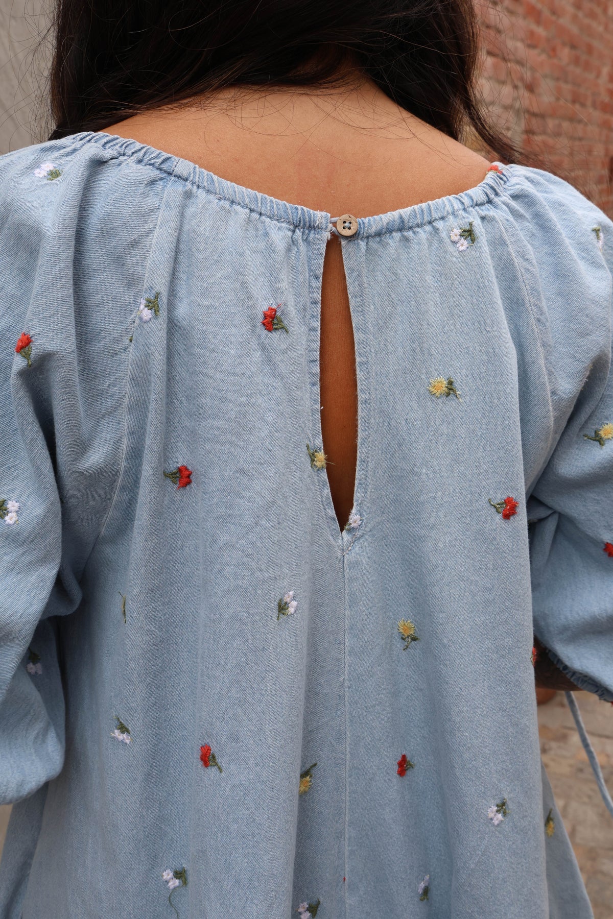 Woman wearing a jean romper with details against grey and brick background