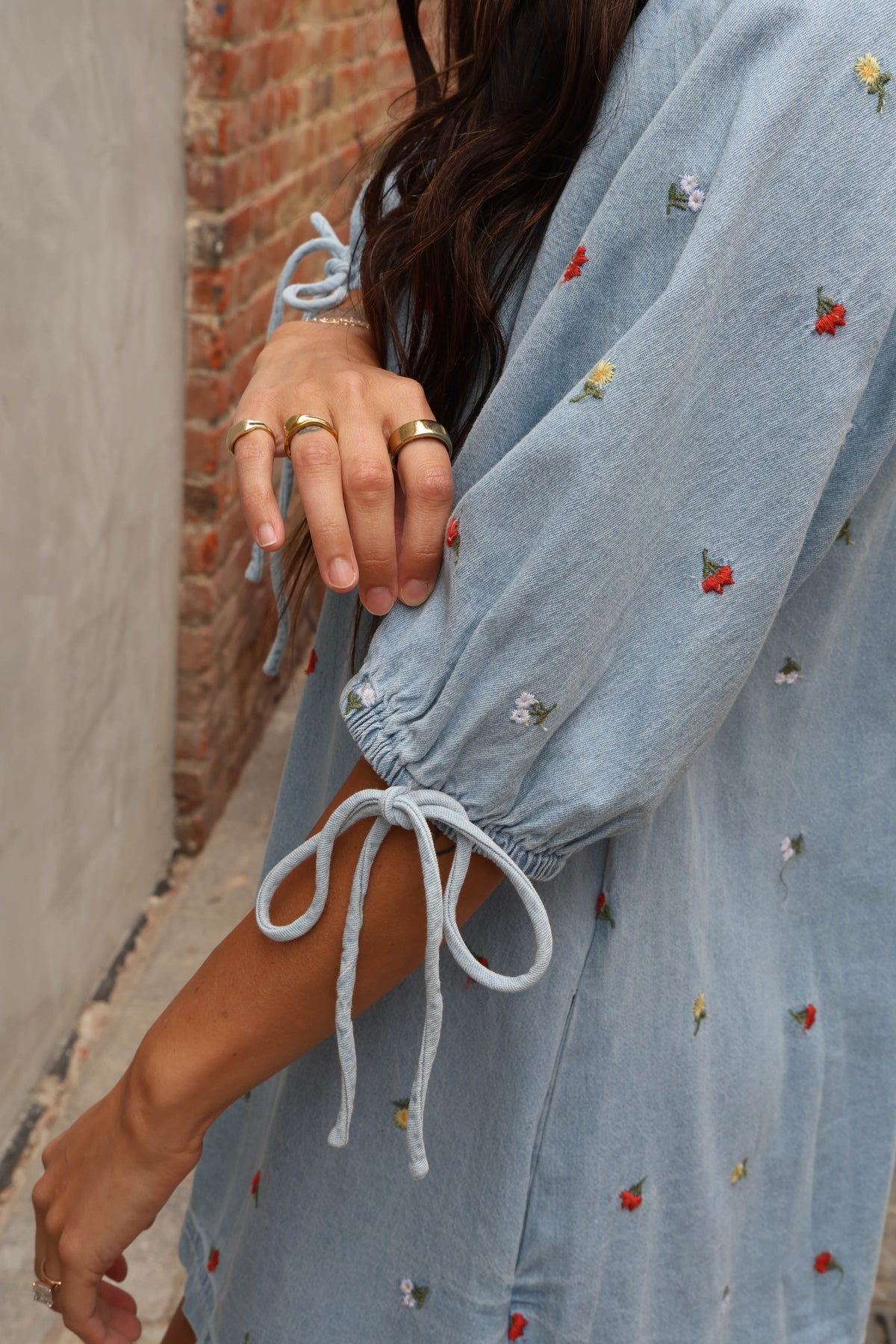 Woman wearing a jean romper with details against grey and brick background