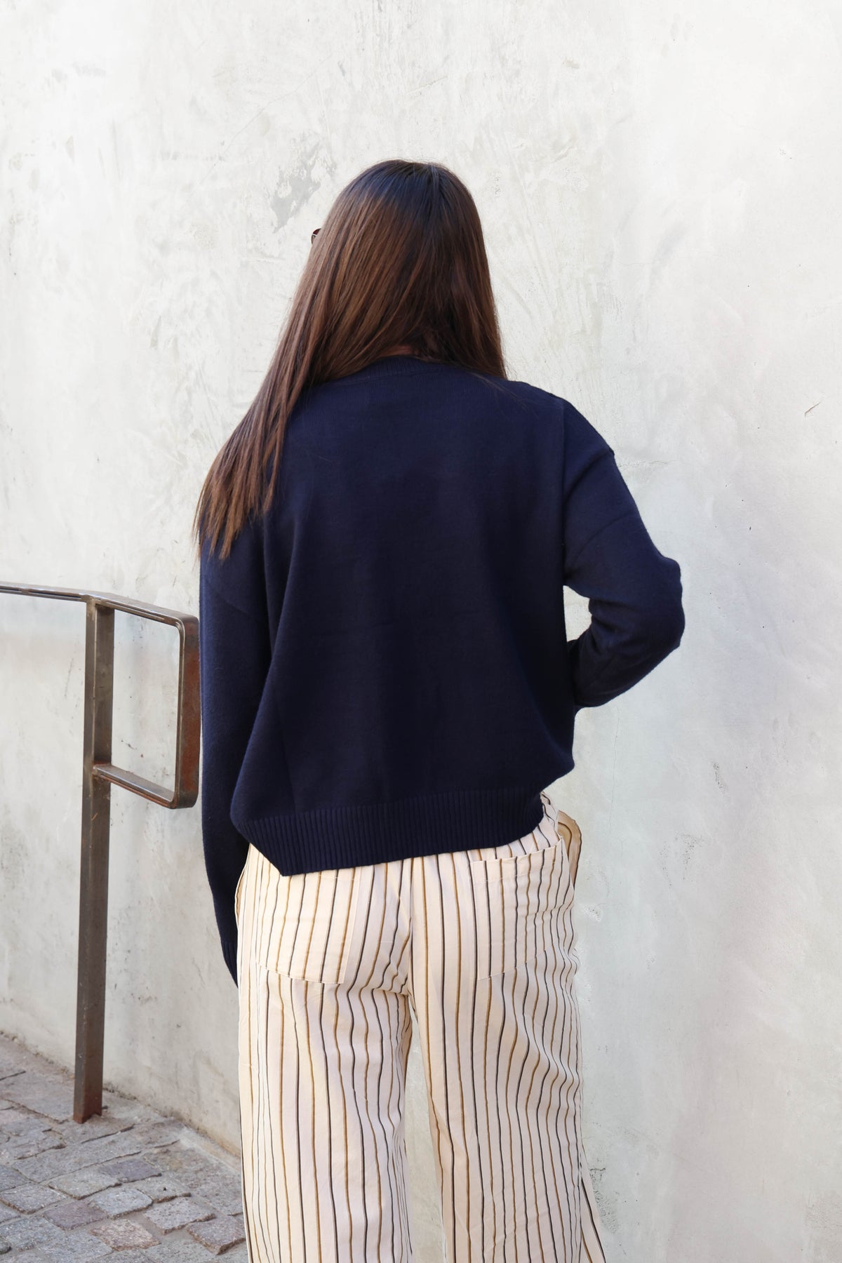 Woman wearing a sweater and striped pants standing in front of a plain wall.