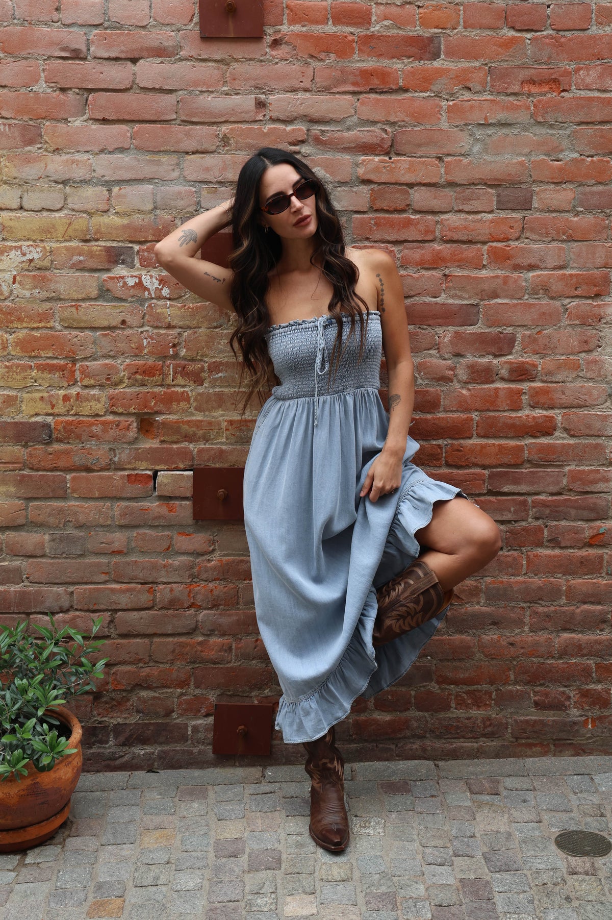 Woman in a strapless dress and boots standing against a brick wall.